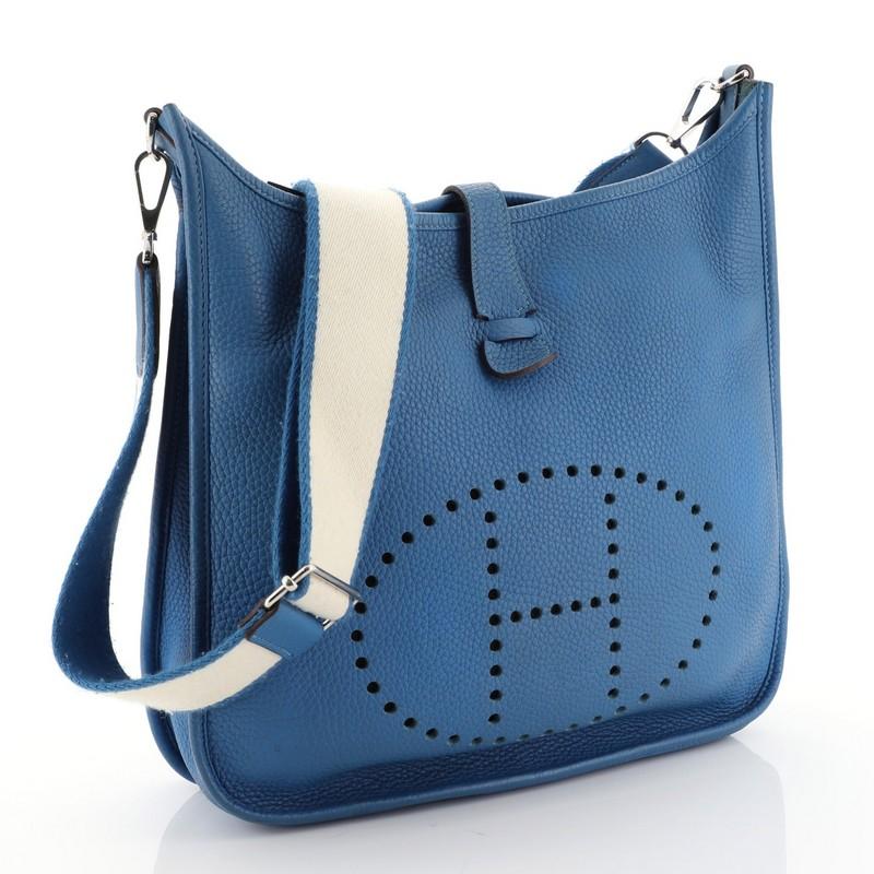 This Hermes Evelyne Crossbody Gen III Clemence PM, crafted in Mykonos blue Clemence leather, features perforated H design at the front, accessible back pocket, Blanc Amazone shoulder strap, and palladium hardware. It opens to a Mykonos blue raw