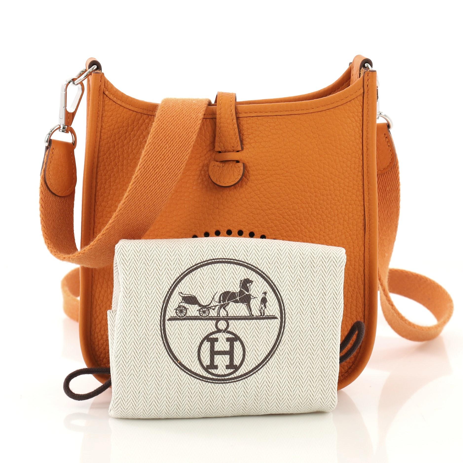 This Hermes Evelyne Crossbody Gen III Clemence TPM, crafted in Abricot orange Clemence leather, features perforated H design at the front, canvas shoulder strap, and palladium hardware. It opens to an Abricot orange raw leather interior. Date stamp