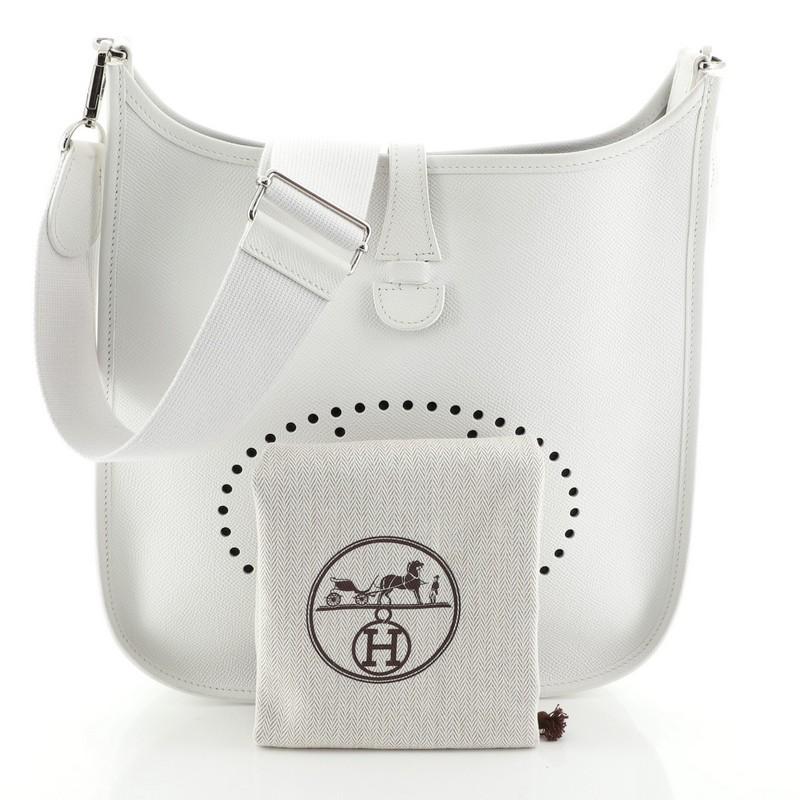 This Hermes Evelyne Crossbody Gen III Epsom PM, crafted in Blanc white Epsom leather, features perforated H design at the front, exterior back pocket, adjustable textile shoulder strap, and palladium hardware. It opens to a Blanc white raw leather