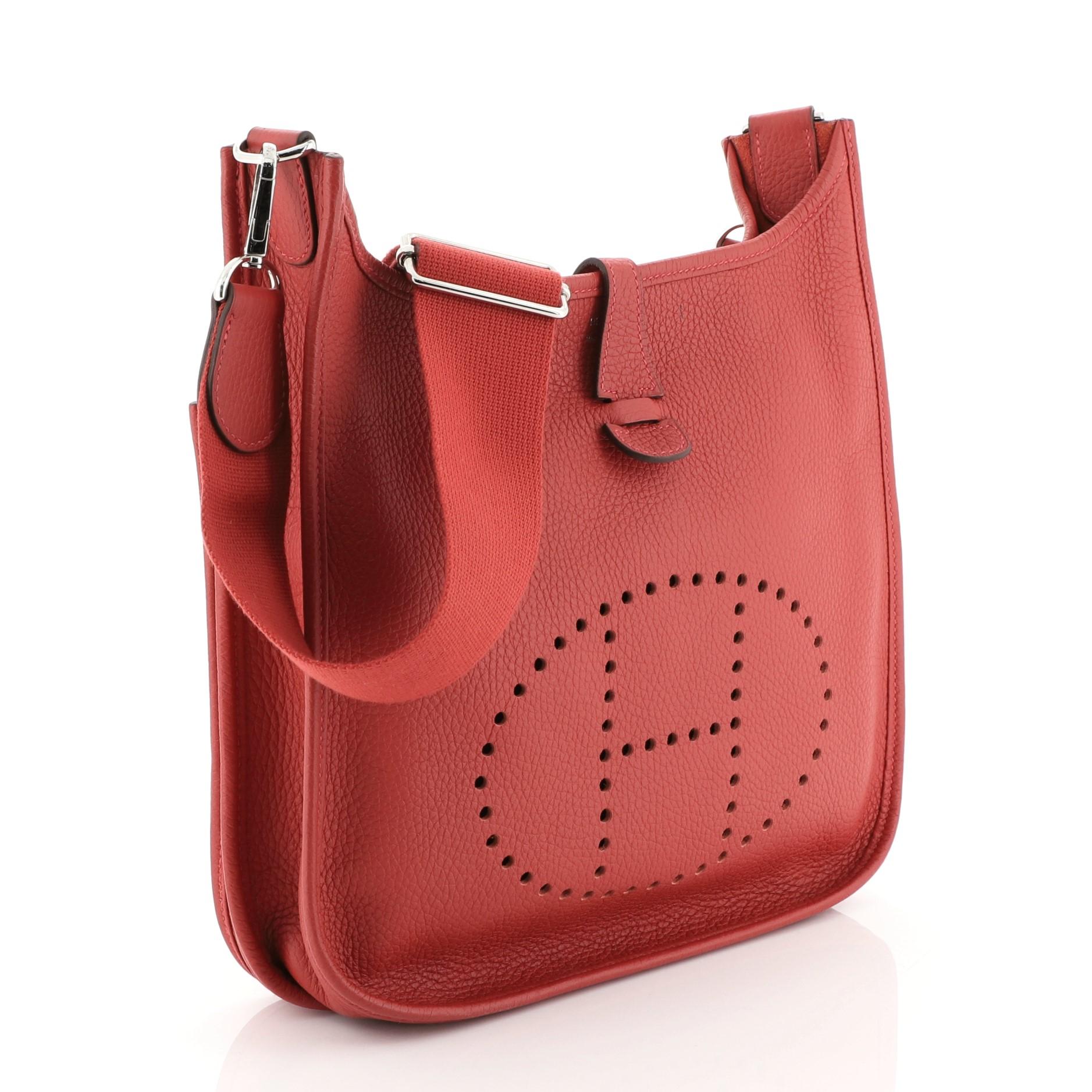 This Hermes Evelyne Crossbody Gen III Togo PM, crafted in Rouge Casaque red Clemence leather, features perforated H design at the front, accessible back pocket, adjustable textile shoulder strap, and palladium hardware. It opens to a Rouge Casaque