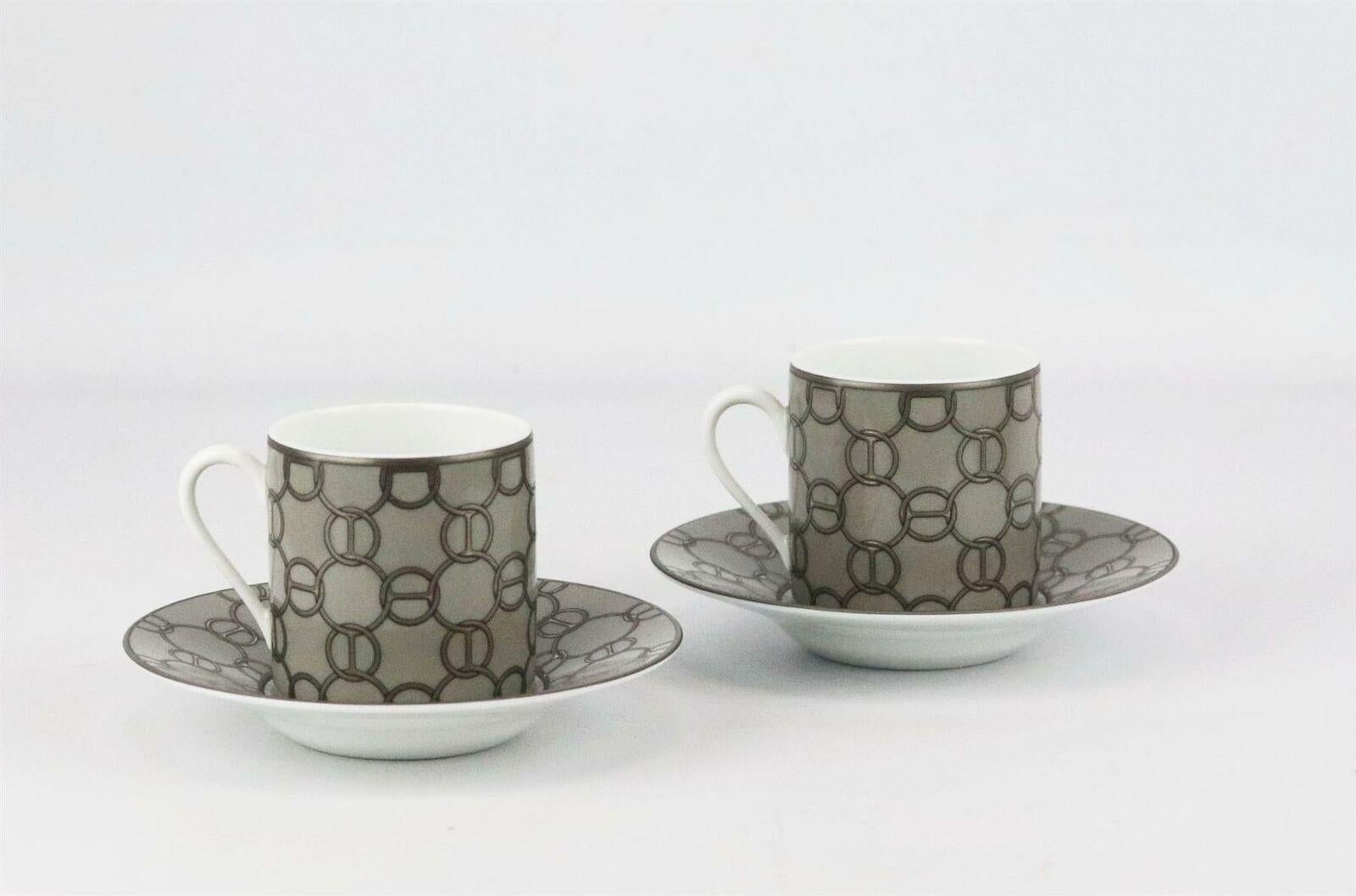 Ensemble de 2 tasses à café et soucoupes assorties Hermès Fil d'Argent en porcelaine grise, argentée et blanche, avec un motif de chaînette sur toute la surface, des accents dorés et le tampon de la marque sur le fond.
Ne vient pas avec la