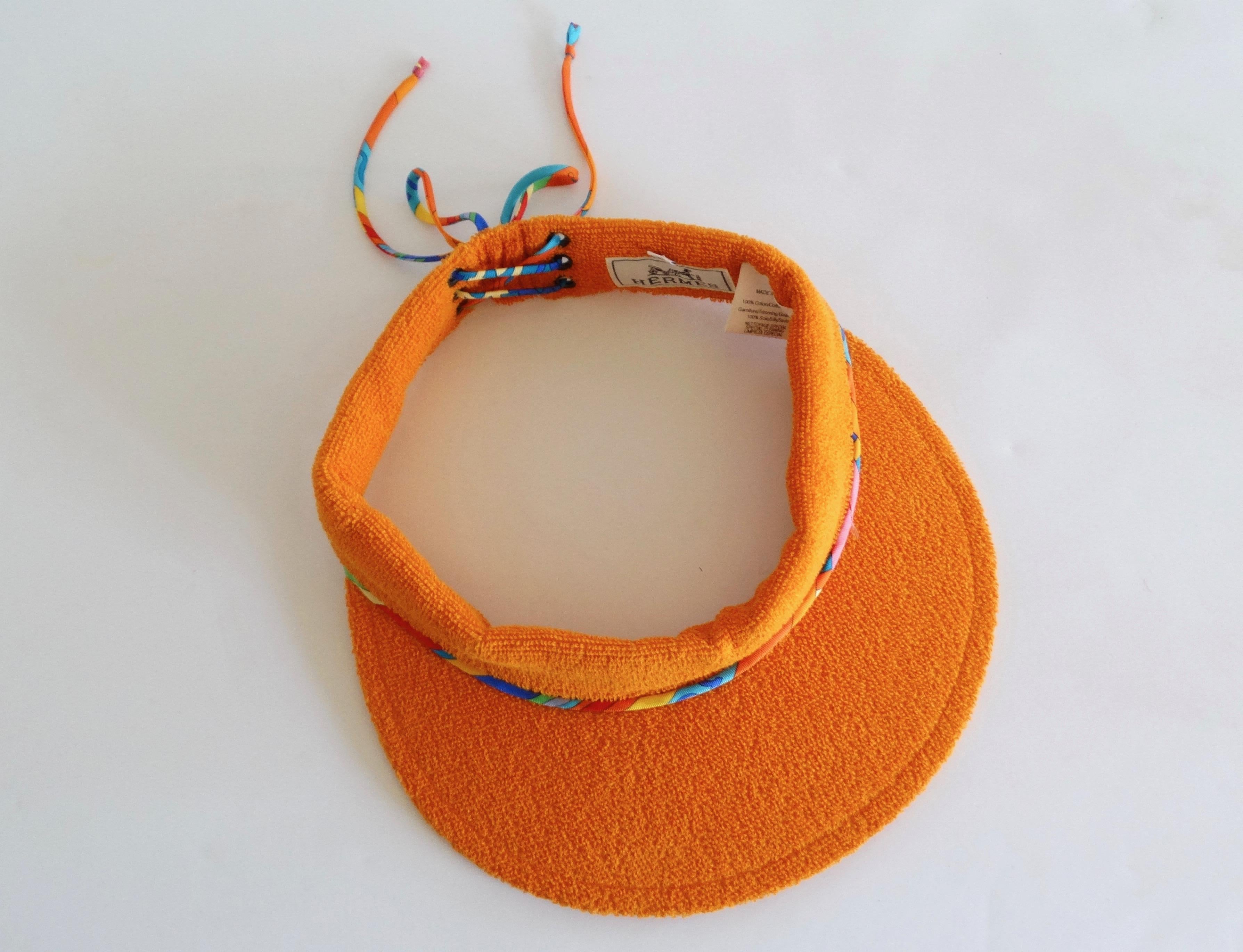 Stay chic while keeping those sun rays off your face with our lovely Hermès Paris Terry sun visor. From their Casquette Oasis collection, this visor is in Laterite (Hermès orange) with a silk twisted multi color lace up back detail. Sz 57 Head