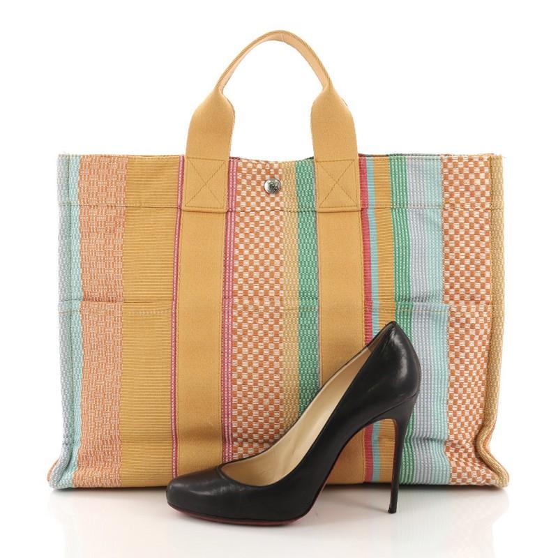This Hermes Fourre Tout Handbag Multicolor Toile MM, crafted in Multicolor Toile, features dual top handles and Palladium hardware. Its snap closure opens to a Jaune yellow Canvas interior. **Note: Shoe photographed is used as a sizing reference,