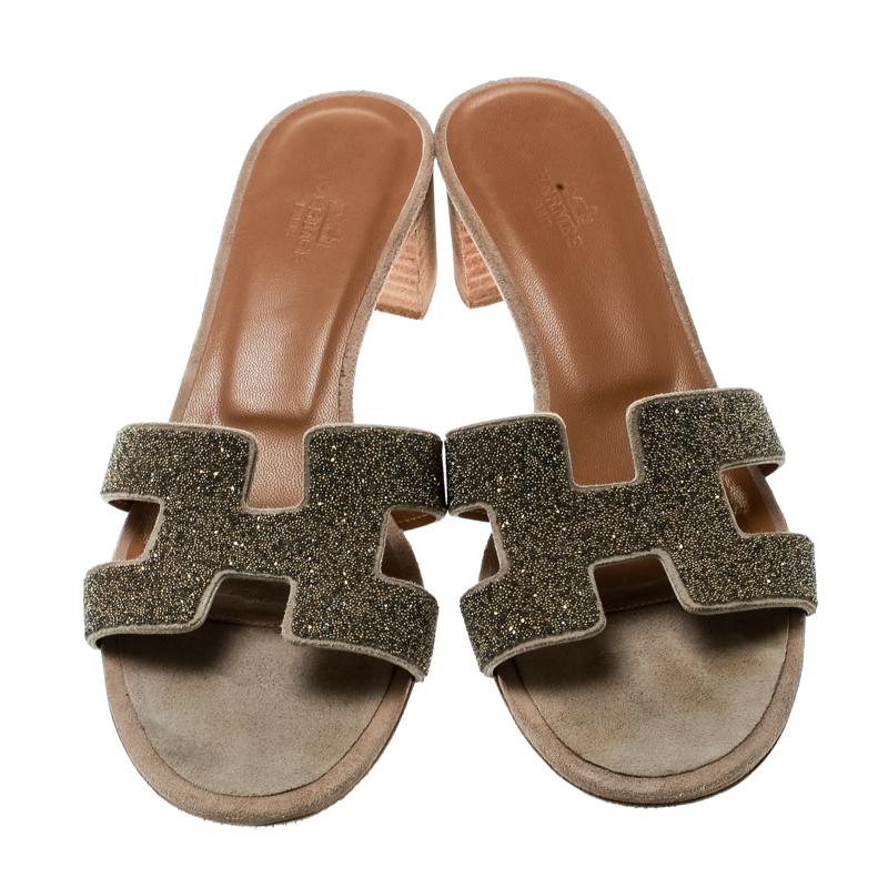 Crafted in gold glitter leather, these Oasis slide sandals from Hermes are classy and comfortable with their wood-finished 4.5 cm block heels. These slides feature the signature H-shaped straps on the front. The insoles are lined with leather and