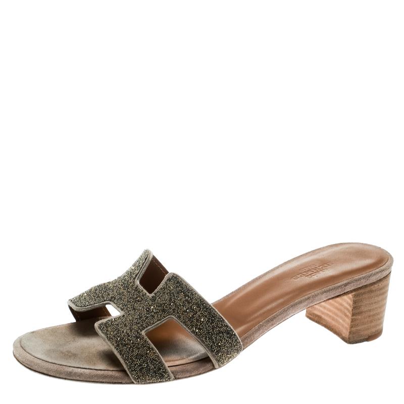 Crafted in gold glitter leather, these Oasis slide sandals from Hermes are classy and comfortable with their wood-finished 4.5 cm block heels. These slides feature the signature H-shaped straps on the front. The insoles are lined with leather and