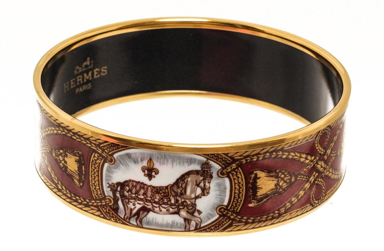 Hermes gold hardware Email bangle with black on the inside, a Hermes Paris logo, and graphics of horses, ropes, and tassels around the exterior of the bangle.


84925MSC