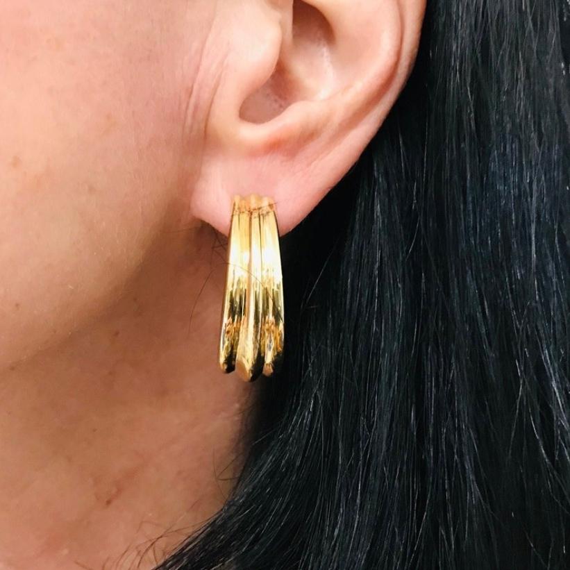 Made from polished yellow gold, the design of these Hermes oval hoop earrings plays with soft curves and clean lines. Each earring features three raised ridges running parallel along the surface, adding depth and a bit of texture. The rounded