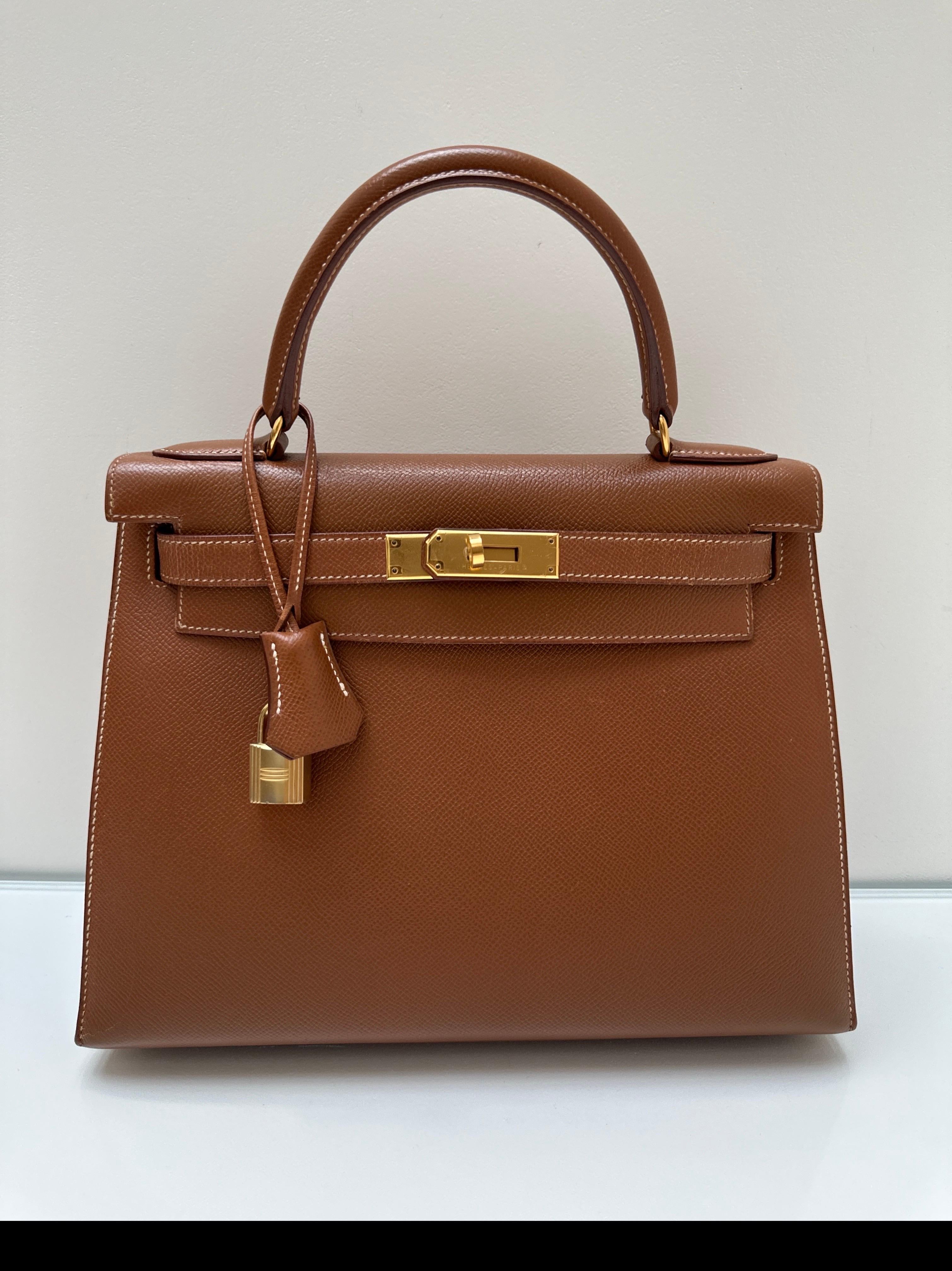 Sac Hermes Kelly 28 en or. La couleur la plus recherchée est le bronzage doré avec des surpiqûres blanches contrastées. Sac sellier doré avec accessoires dorés. Nettoyage intérieur. Excellent état. Comprend une clochette, un cadenas, des clés et un