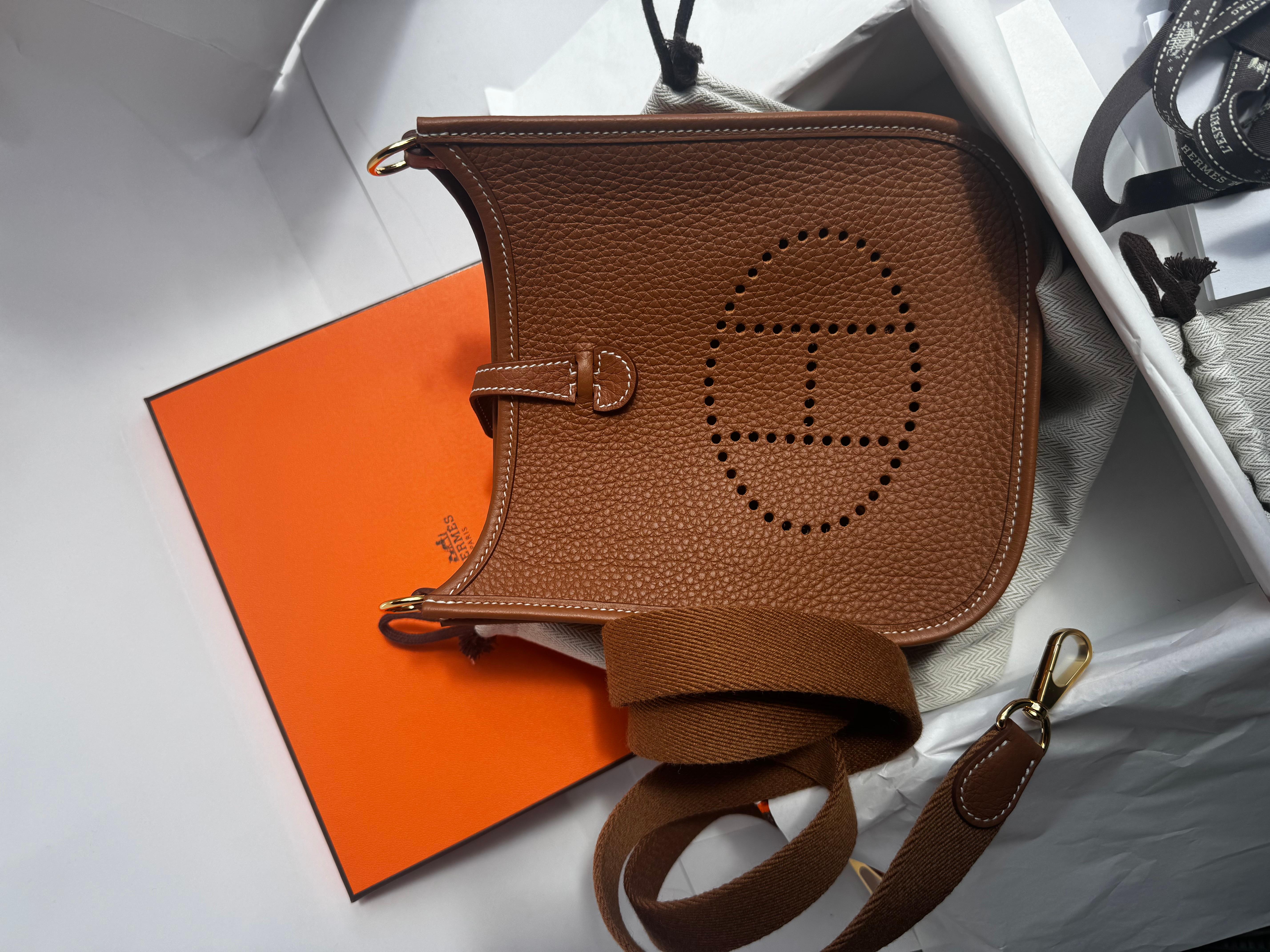 Hermès mini Evelyne in gold Clemence leather complemented with gold-tone hardware and white stitching. It features a perforated 