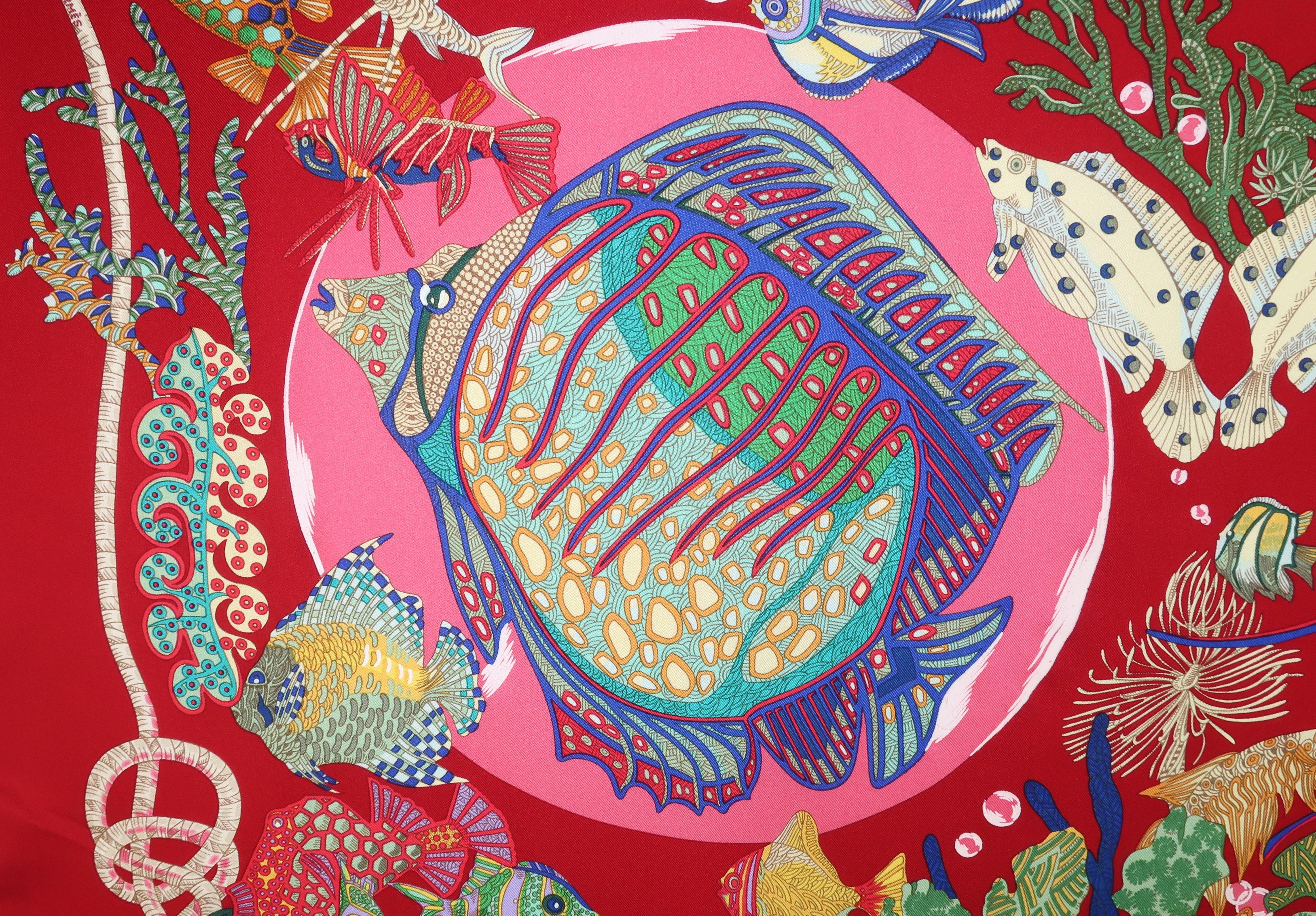An enchanting 1992 silk scarf design by artist, Annie Faivre, for Hermès aptly entitled 'Grand Fonds' or 'The Deep Sea'.  A deep cherry red serves as backdrop to large and small fish in various shades of blue, green and yellow with pink and white