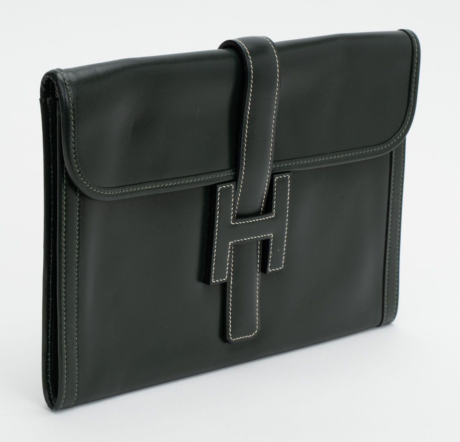 Hermès Jige Clutch Box Kalb . Die Tasche ist in ausgezeichnetem Zustand. Das Äußere besteht aus schwarzem Kalbsleder, das Innere aus einem beigen Leinenstoff. Die Clutch wird mit einem H-Logo-Verschluss geschlossen. Kommt mit originalem