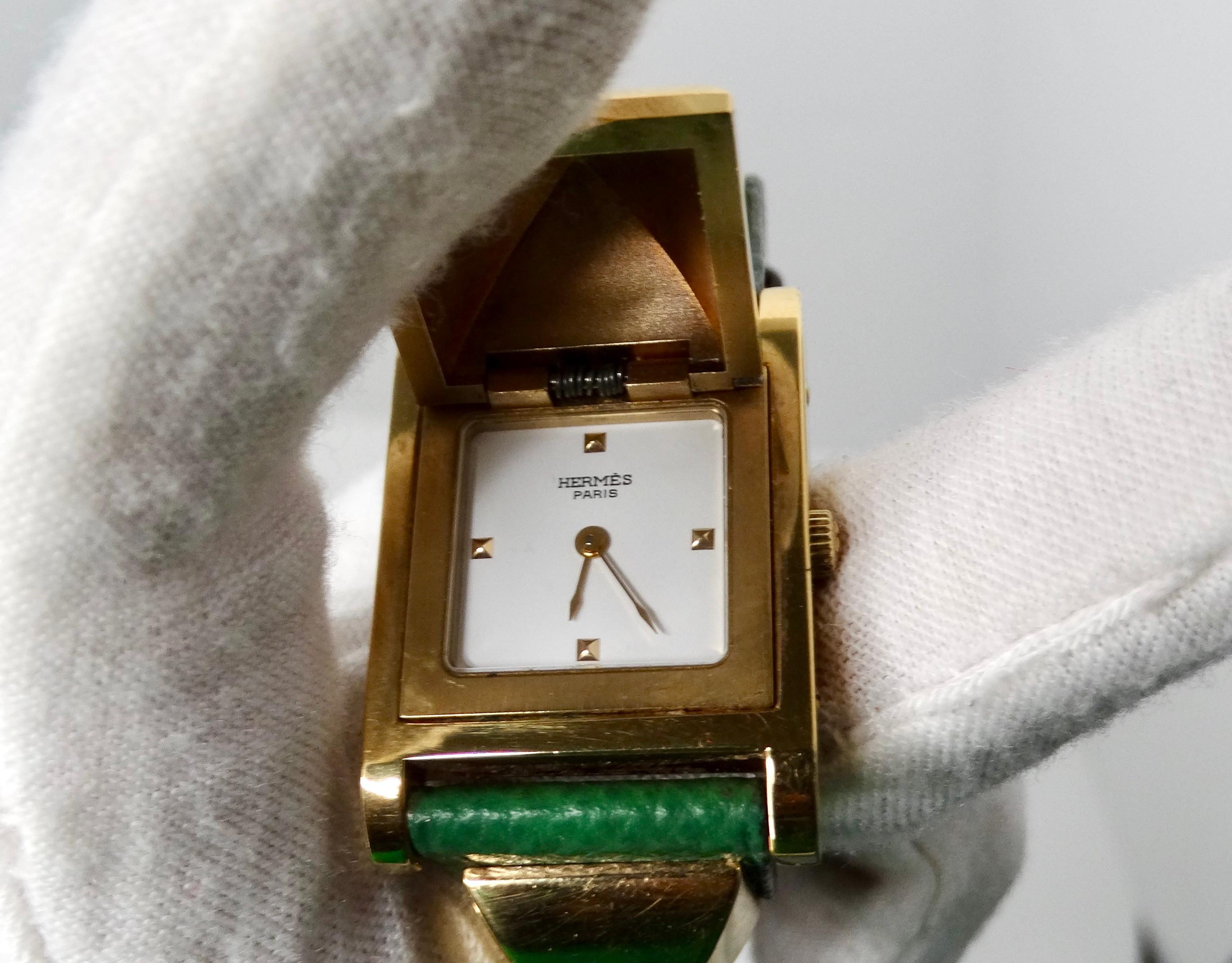 The Hermès Green Medor 23mm Leather & Stainless Steel Watch is a luxurious timepiece that exemplifies elegance and craftsmanship. The watch features a striking gold-plated rock stud case, with two additional studs on each side that seamlessly blend