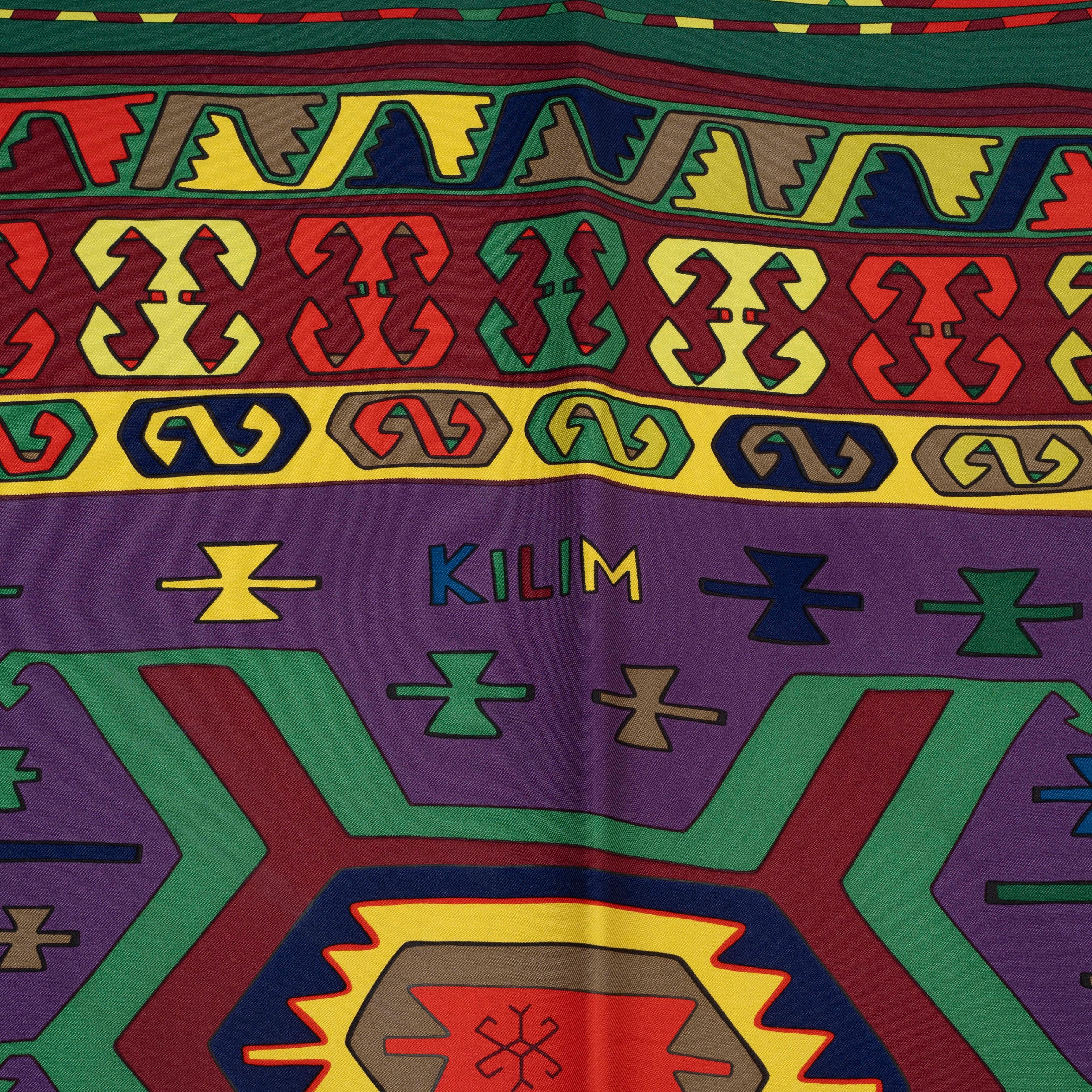 This 100% authentic Hermès Kilim 90 scarf, designed by Dimitri Rybaltchenko, is crafted from luxurious purple silk twill (100%). It features a dark green border and intricate details in burgundy, yellow, and orange, creating a vibrant and artistic