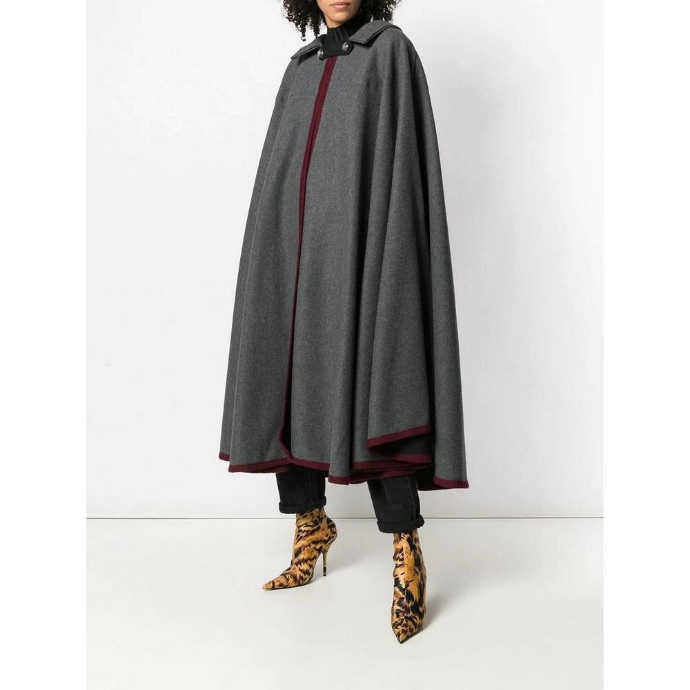 Hermès wide cape in grey wool from the 1990s. The cape is lined with burgundy edges. It features a classic collar and front closure with buttons.