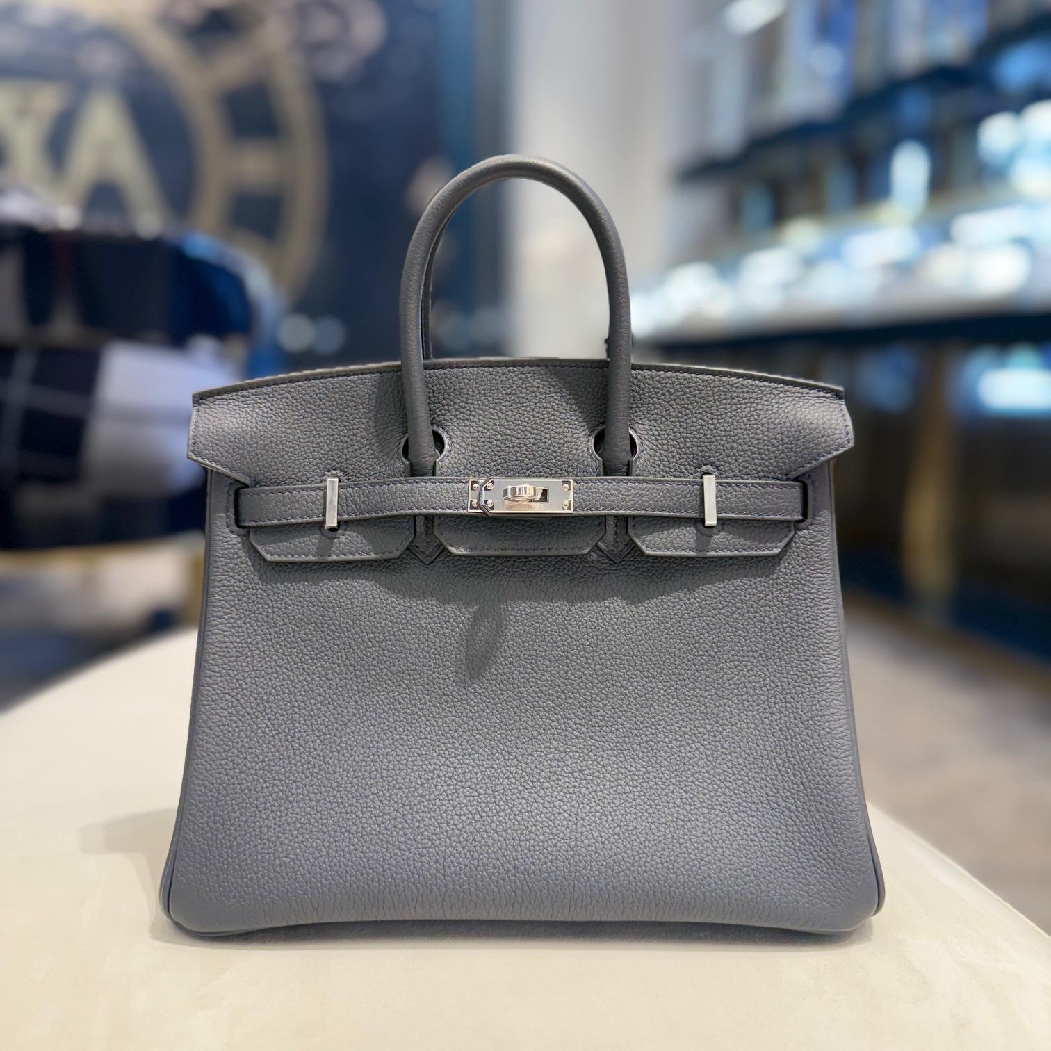 Jewels Aficionado offers an Hermès Gris Misty Birkin 25 in Togo leather that is a timeless and versatile piece. Its soft gray hue complements the classic Birkin silhouette, while Togo leather offers a textured, durable finish with a structured yet