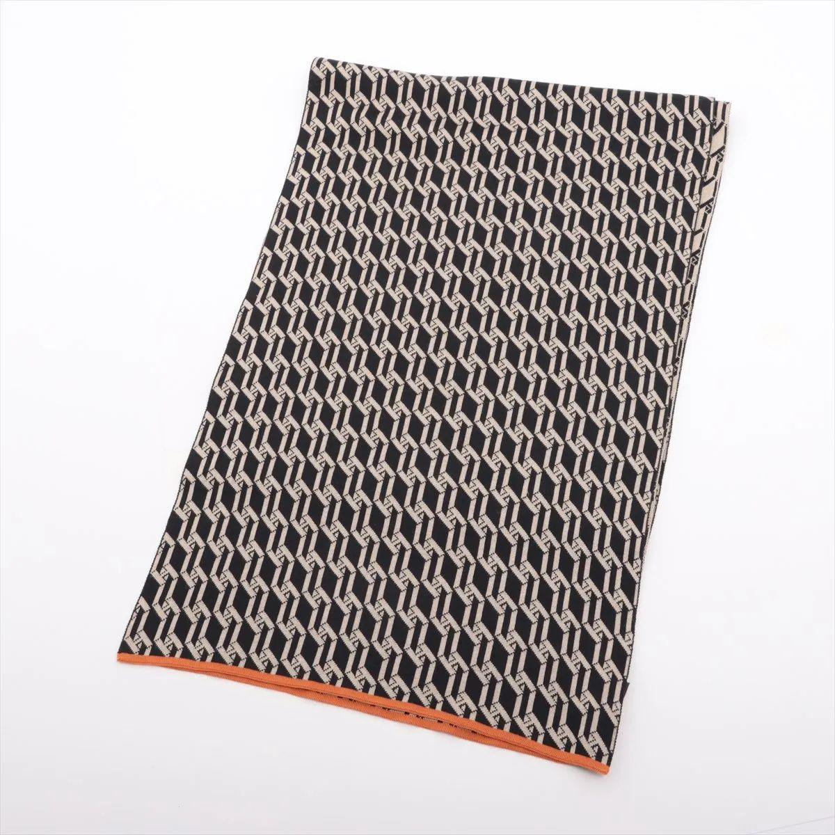 Der Hermès H-Logo-Strickschal in Beige und Schwarz ist ein raffiniertes Accessoire, das klassischen Stil mit modernem Design verbindet. Sie ist aus weicher, hochwertiger Wolle gefertigt und mit einem auffälligen H-Logo-Muster in kontrastierenden