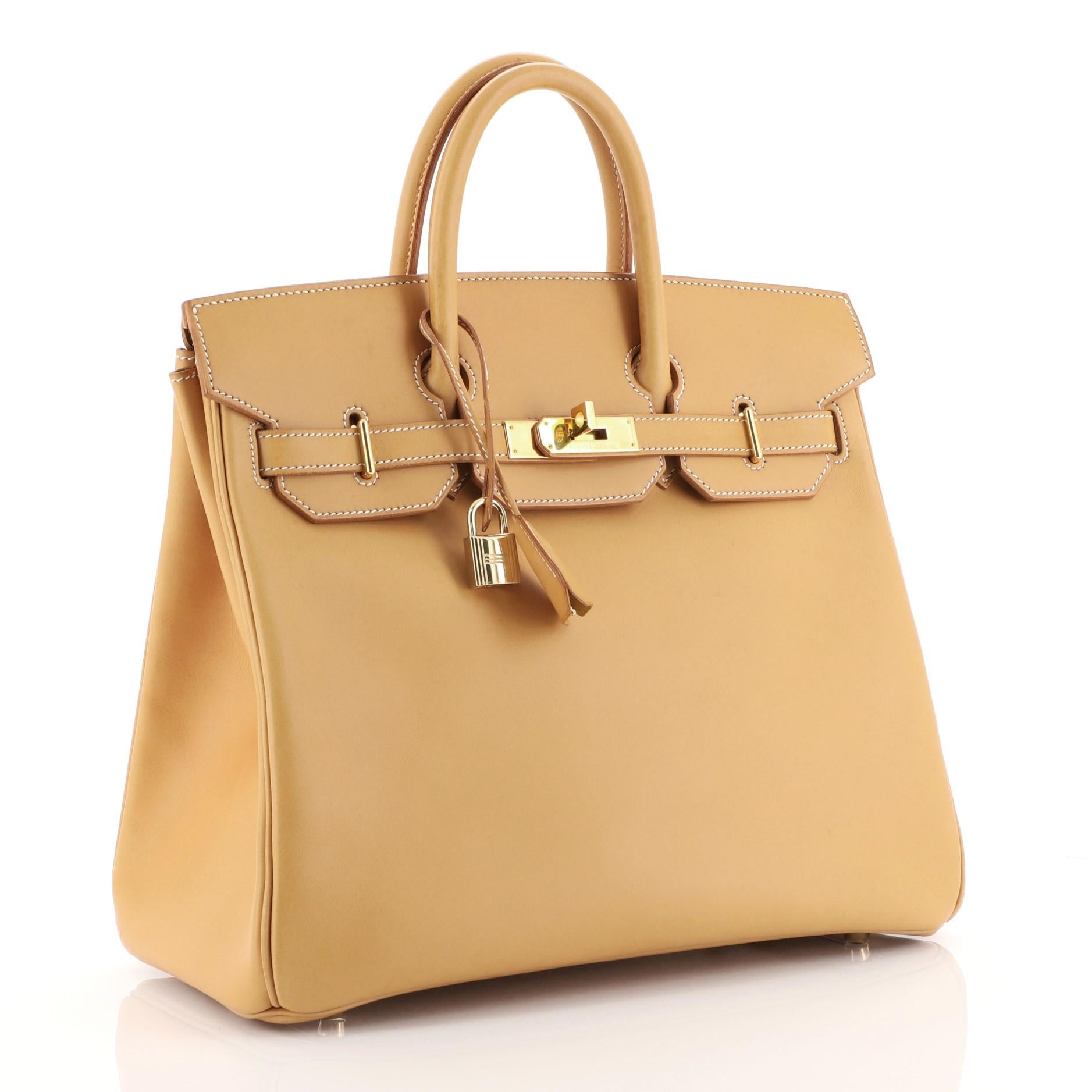 This Hermes HAC Birkin Bag Natural Vache Natural with Gold Hardware 32, crafted in Natural brown Vache Naturelle leather, features dual rolled handles, front flap, and gold hardware. Its turn-lock closure opens to a Natural brown Vache Naturelle