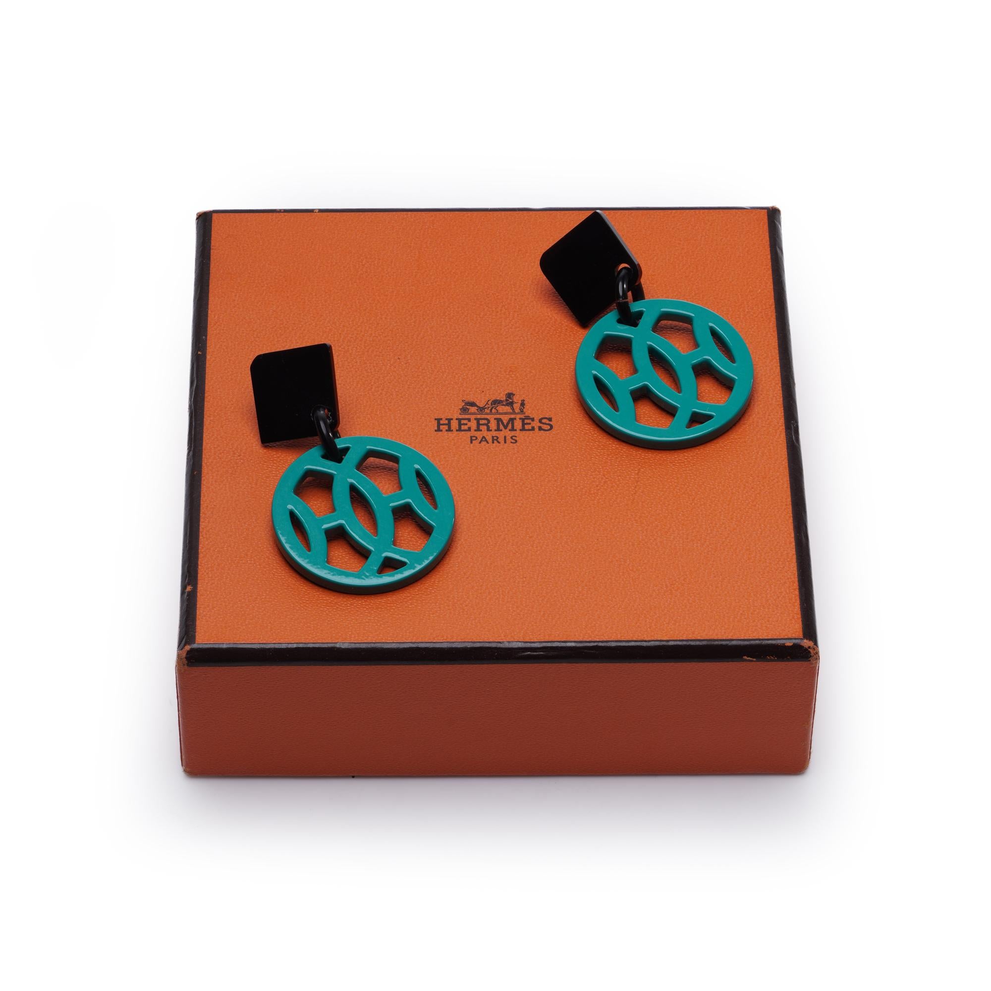 Élégante paire de boucles d'oreilles Havas de la Collection Horn, en métal argenté, ornées de détails en laque et en corne. Les boucles d'oreilles sont composées de gouttes géométriques en laque verte, suspendues à des tops de couleur noire et