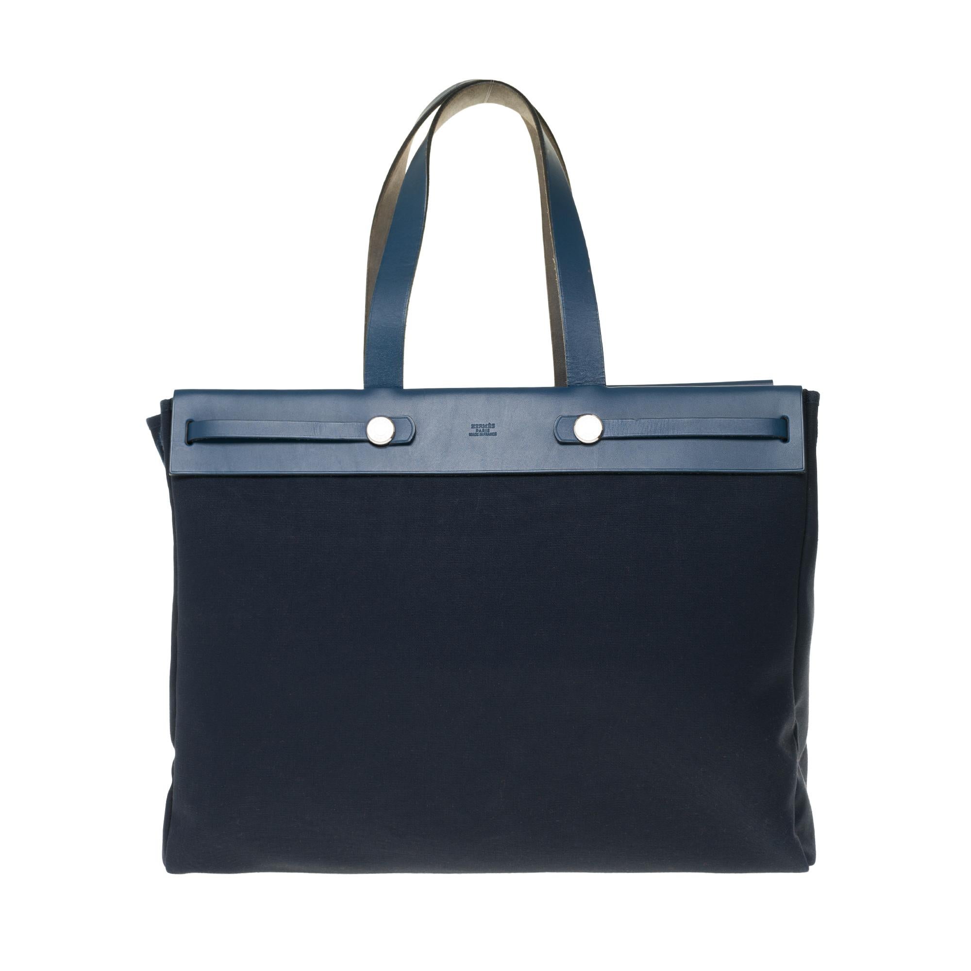 Practical Hermes Herbag GM handbag in navy blue canvas and blue leather, palladium silver metal hardware, blue leather handle, a removable black leather handle allowing a hand or shoulder support.

Strap closure on flap.
A zipped pocket on the back