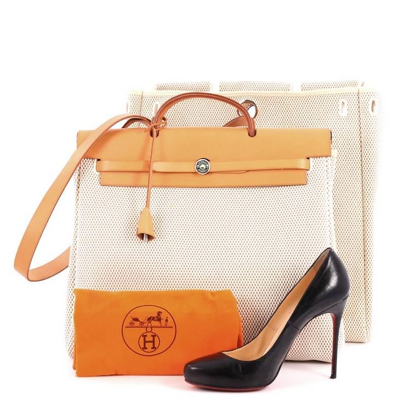 This authentic Hermes Herbag Toile and Leather MM is a fabulously functional Hermes set with two stylishly classic handbags fitting any mood. Constructed from natural beige toile and brown vache hunter leather, this functional interchangeable bag