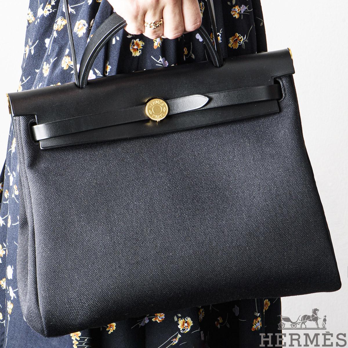 A chic Hermes Herbag Zip 31 handbag. The exterior of this Herbag features a top handle with a crossbody strap in Noir Vache Hunter leather on the top section whereas the body of the bag is made out of Noir Toile Militaire canvas, has a Clou de Selle