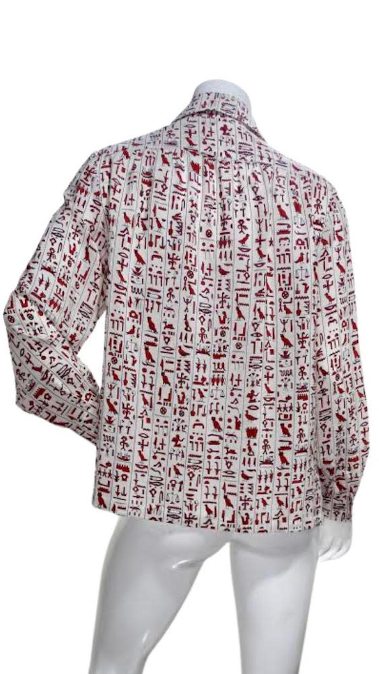 Hello Hermes! Circa 1970s, this Silk Hermes button up blouse features red Egyptian hieroglyphics outlined with blue all throughout with cuffed long sleeves. Simple and timeless, this blouse is perfect to pair with your Kelly bag and favorite pair of