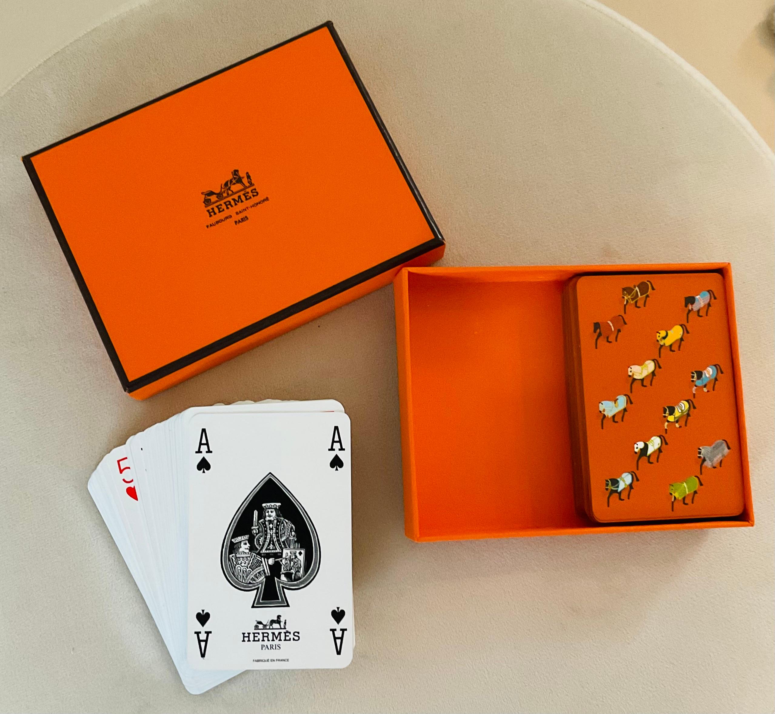 Un raffinato set di carte da gioco vintage di Hermès Paris con due mazzi presentati nella scatola arancione tipica del marchio. Ciascuna coperta presenta il classico motivo del cavallo di Hermès, una in un ricco marrone e l'altra in un verde