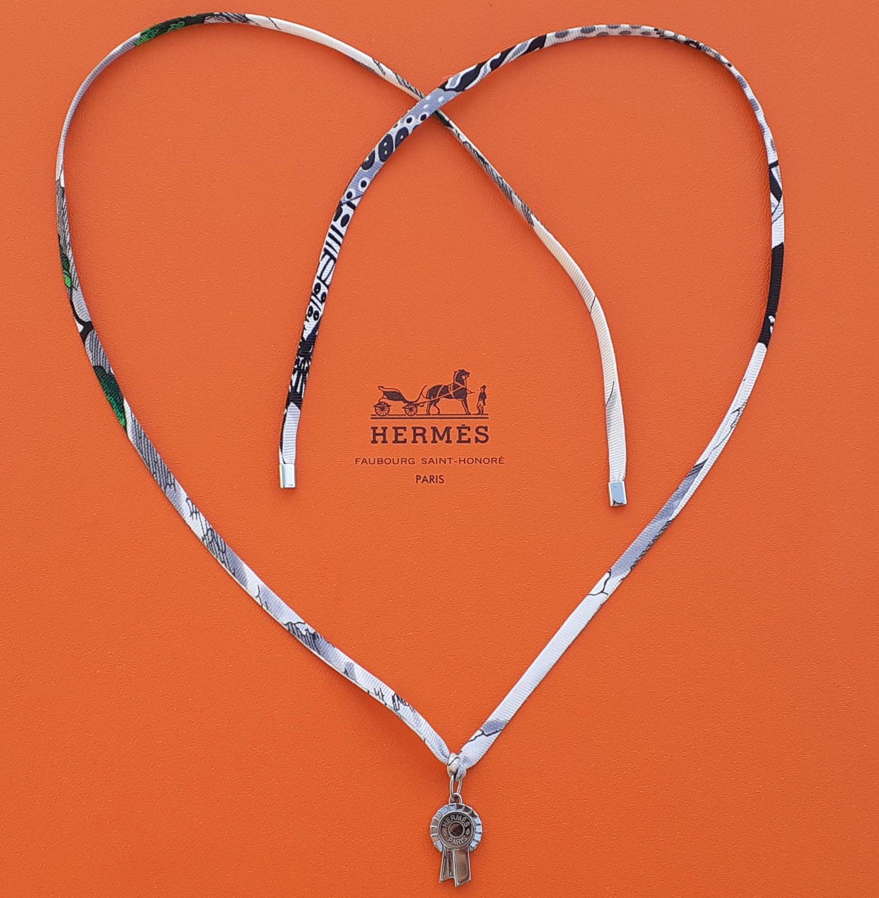 Cute Authentic Hermès Necklace

Pendant in shape of a horse show ribbon

Necklace made of silk / Pendant made of palladium plated hardware (silver-tone)

Pendant can be removed from the silk link and used as a charm

Top of the pendant is in shape