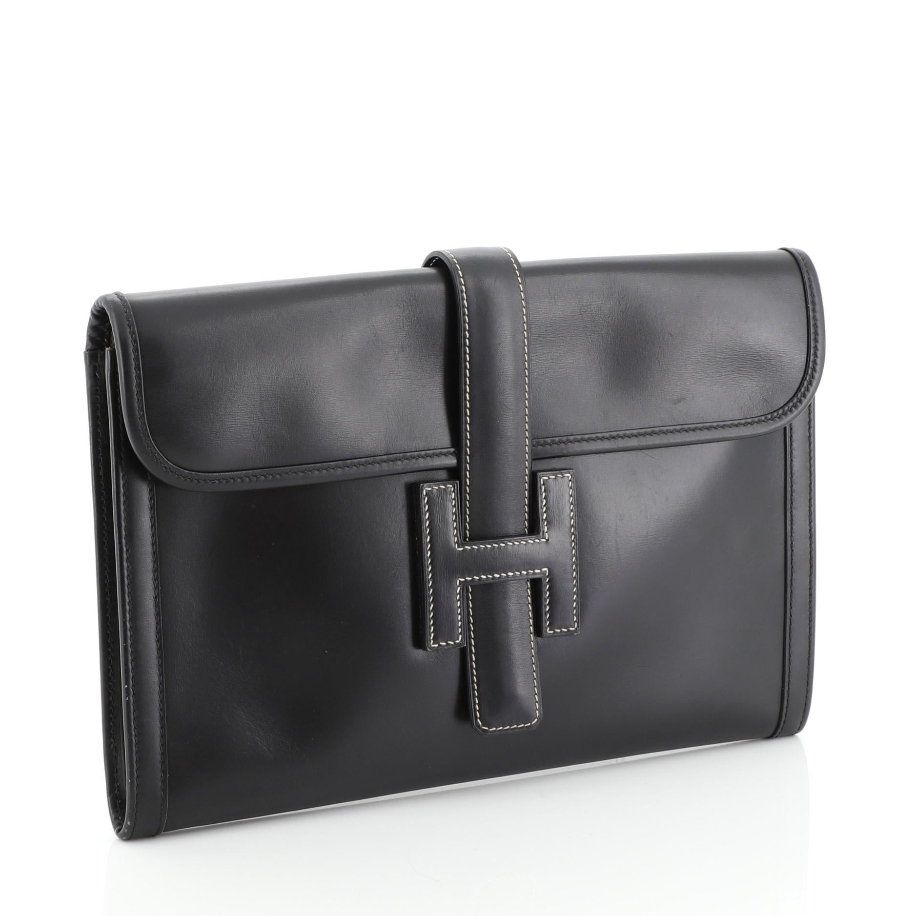 This Hermes Jige Clutch Box Calf PM, crafted in Noir black Box Calf leather, features a cross-over flap and strap that tucks under the logo H. It opens to an Ecru neutral Toile H interior. Date stamp reads: Y Circle (1995). 

Estimated Retail Price: