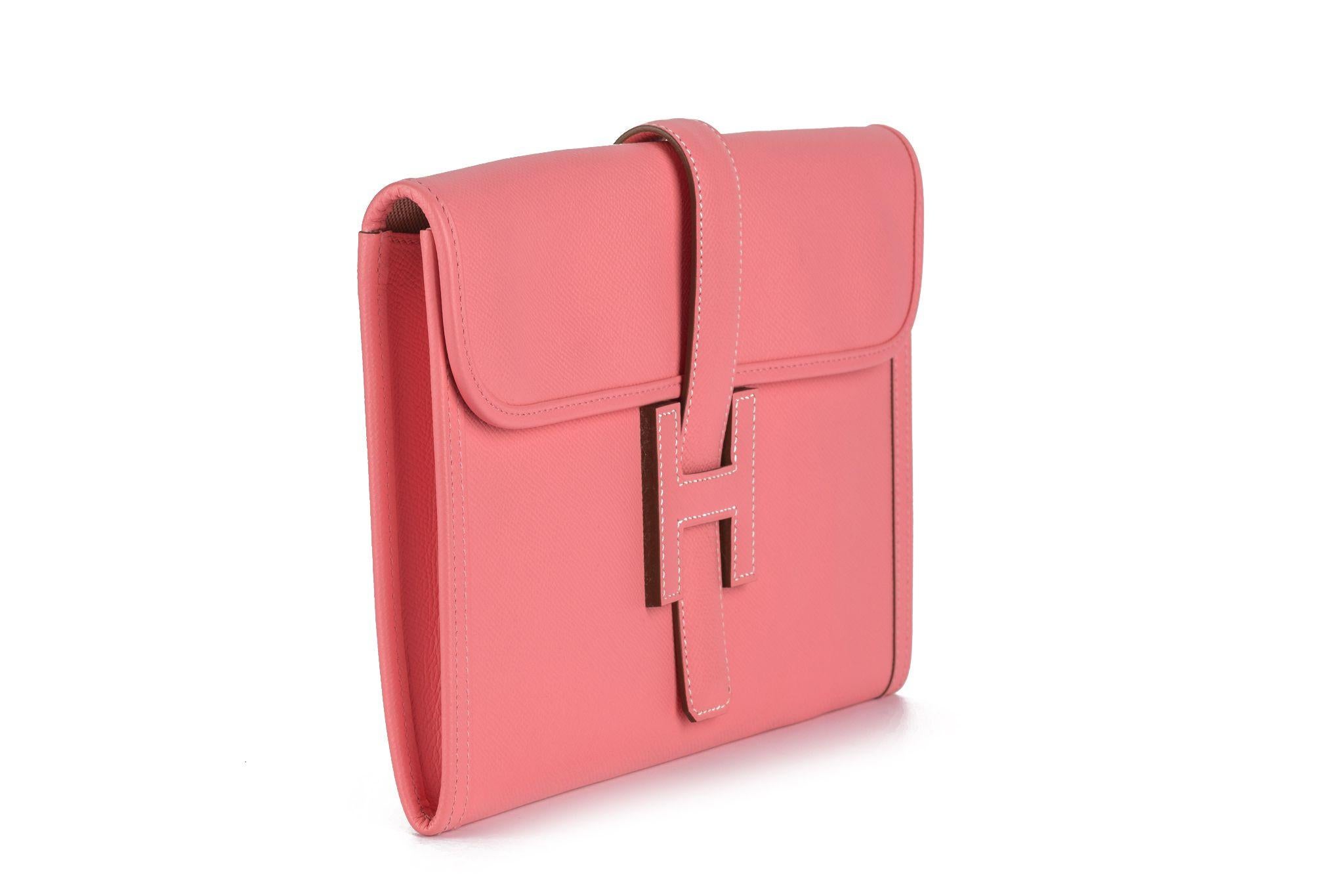 This Hermès Jige Elan 29 Clutch in rose confetti  is crafted of luxurious epsom leather. There is a cross-over flap and a strap that tucks under a leather Hermès 