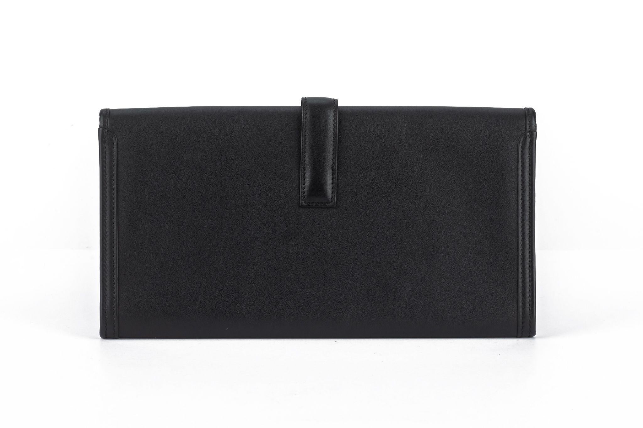 This Hermès Swift Jige Elan 29 Clutch in black features swift calfskin leather in black. It features a cross-over flap with a strap that tucks under a leather Hermes 