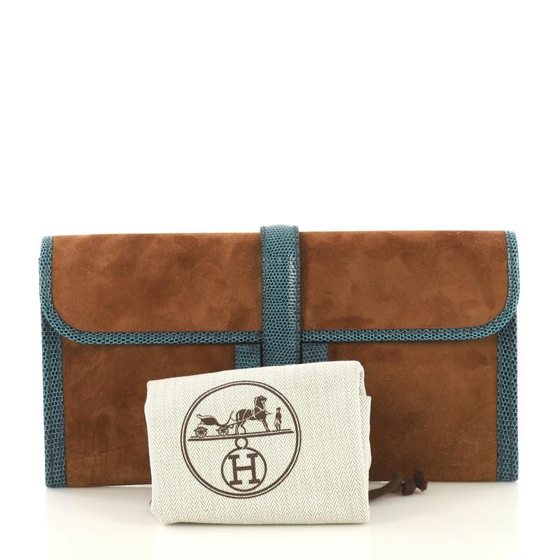 This Hermes Jige Elan Clutch Doblis Suede with Lizard 29, crafted in Fauve brown eau Doblis Suede and Petrole teal Niloticus Lizard, features a cross-over flap and strap that tucks under the logo H. It opens to a Fauve brown Agneau leather interior.