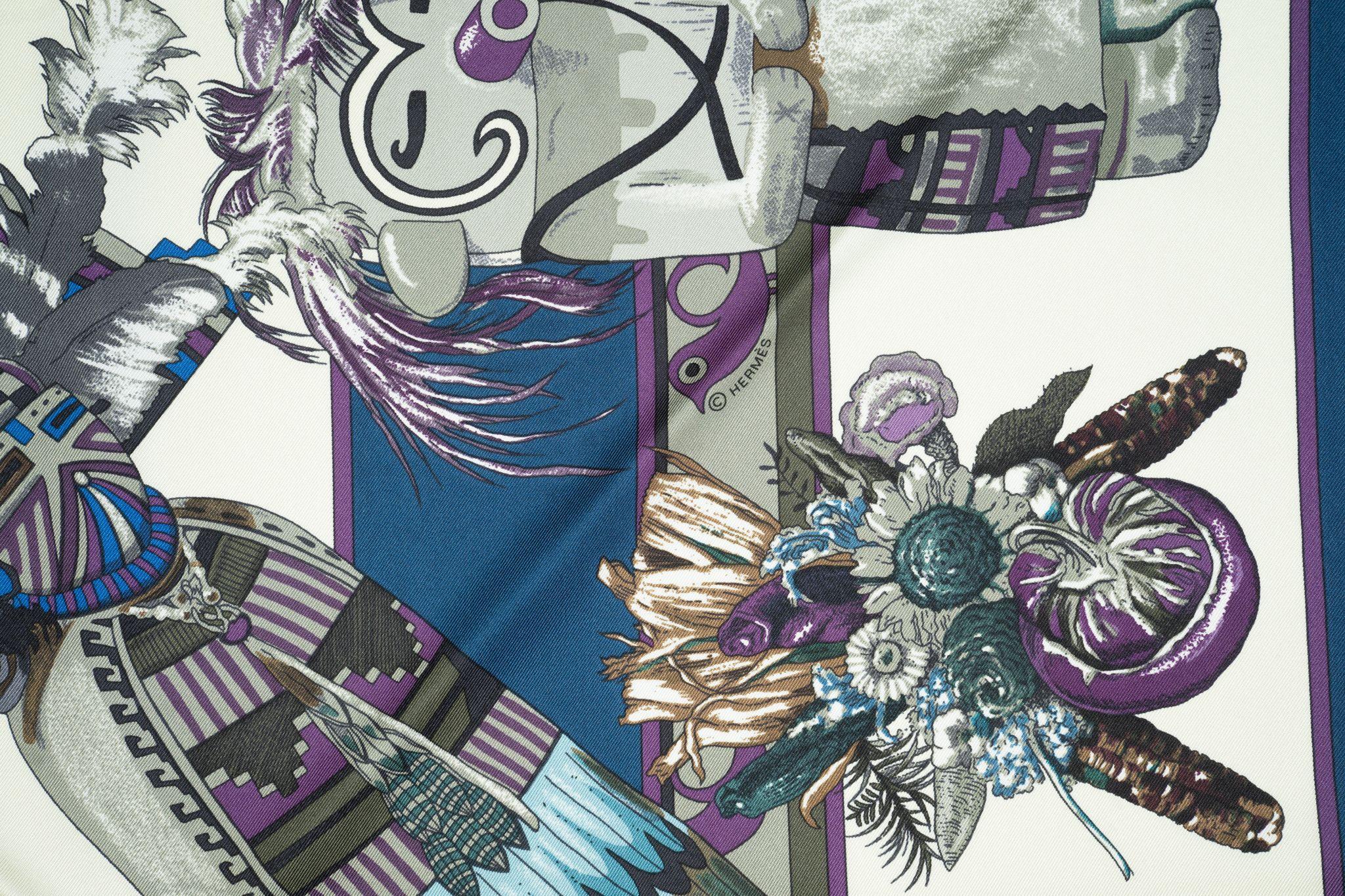 Questa sciarpa a triangolo Hermès Silk Kachina in Marin, Grey Bleu Glacier. Questa elegante sciarpa a triangolo in 100% seta presenta bambole Kachina dai colori vivaci su uno sfondo bianco. Viene fornito con la scatola originale.