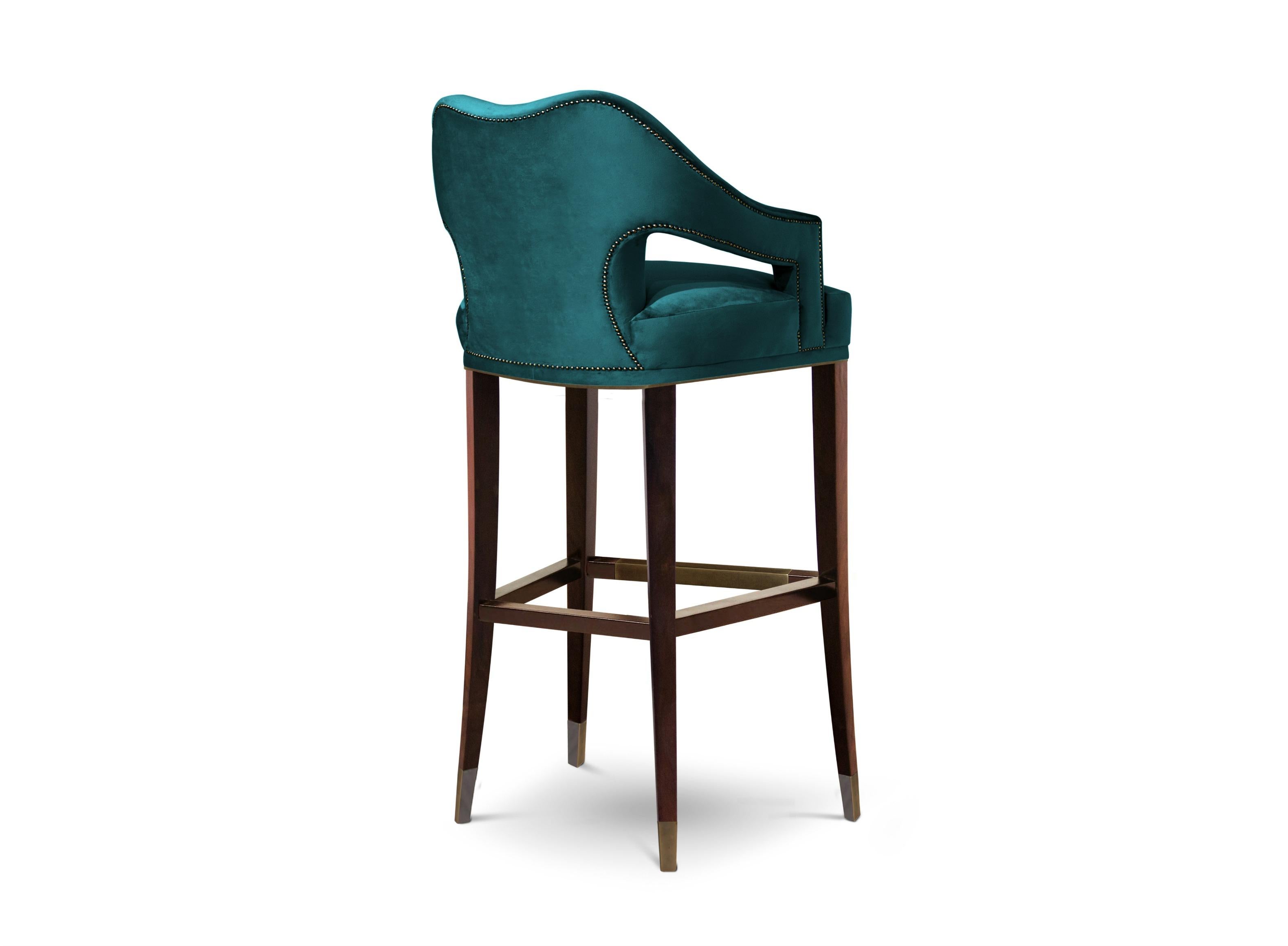 Symbol of knowledge and rebirth, Nº20 Counter Stool was raised through a long journey of 24 prototypes. This fabric chair, upholstered in twill and with legs in ash with walnut stain matte varnish, features a nailhead trim that adds subtle