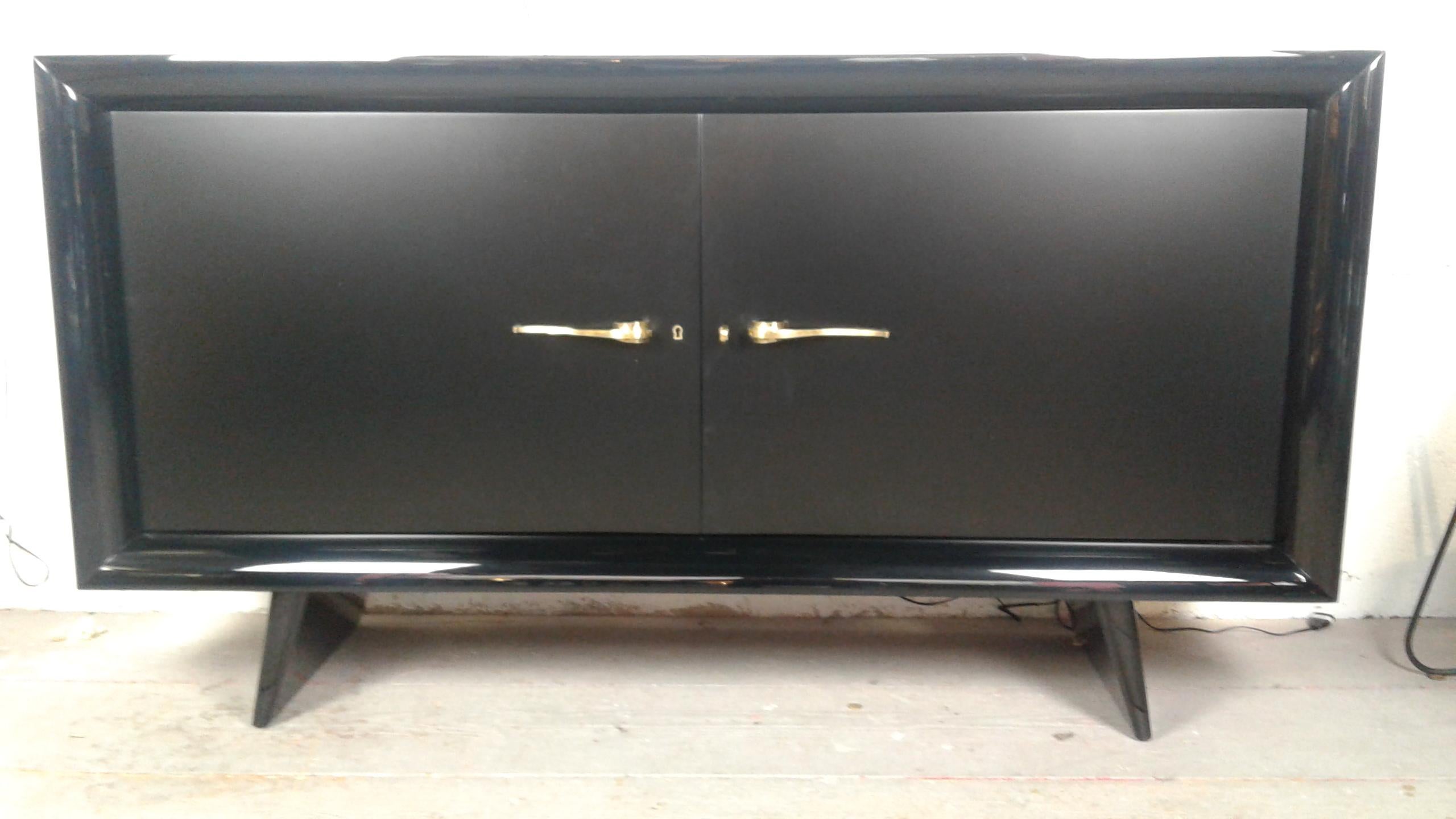 Sideboard in black lacquered wood, composed of a rectangular box with black lacquer, resting on two black lacquered solid feet slightly inclined.
Opening in the middle by two doors in satin black lacquer, the door frames are slightly curved giving