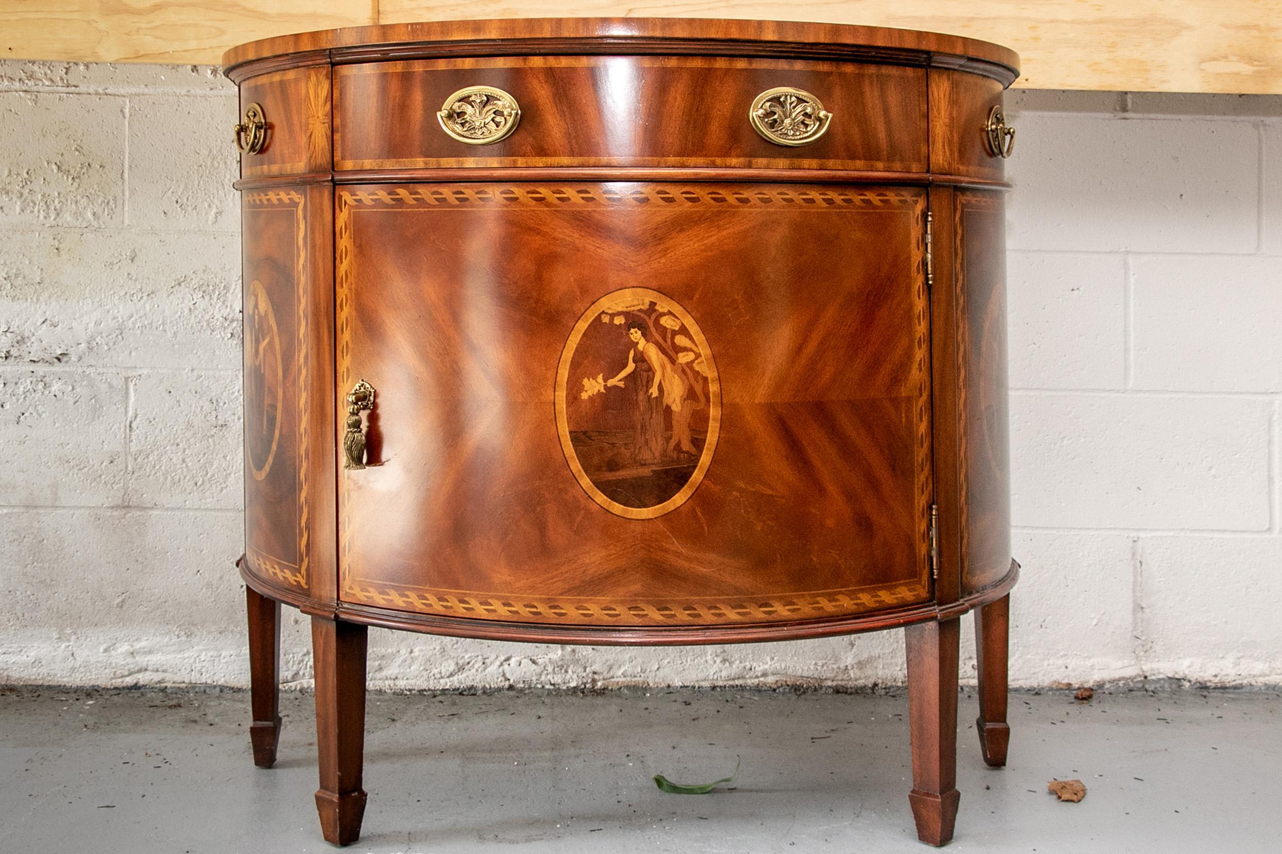 Maitland-Smith burled wood demilune commode, banded top, an apron with a center drawer and two faux side drawers. The lower cabinet with a center door opening to a single shelf. Both door and sides with marquetry panels with neoclassical female