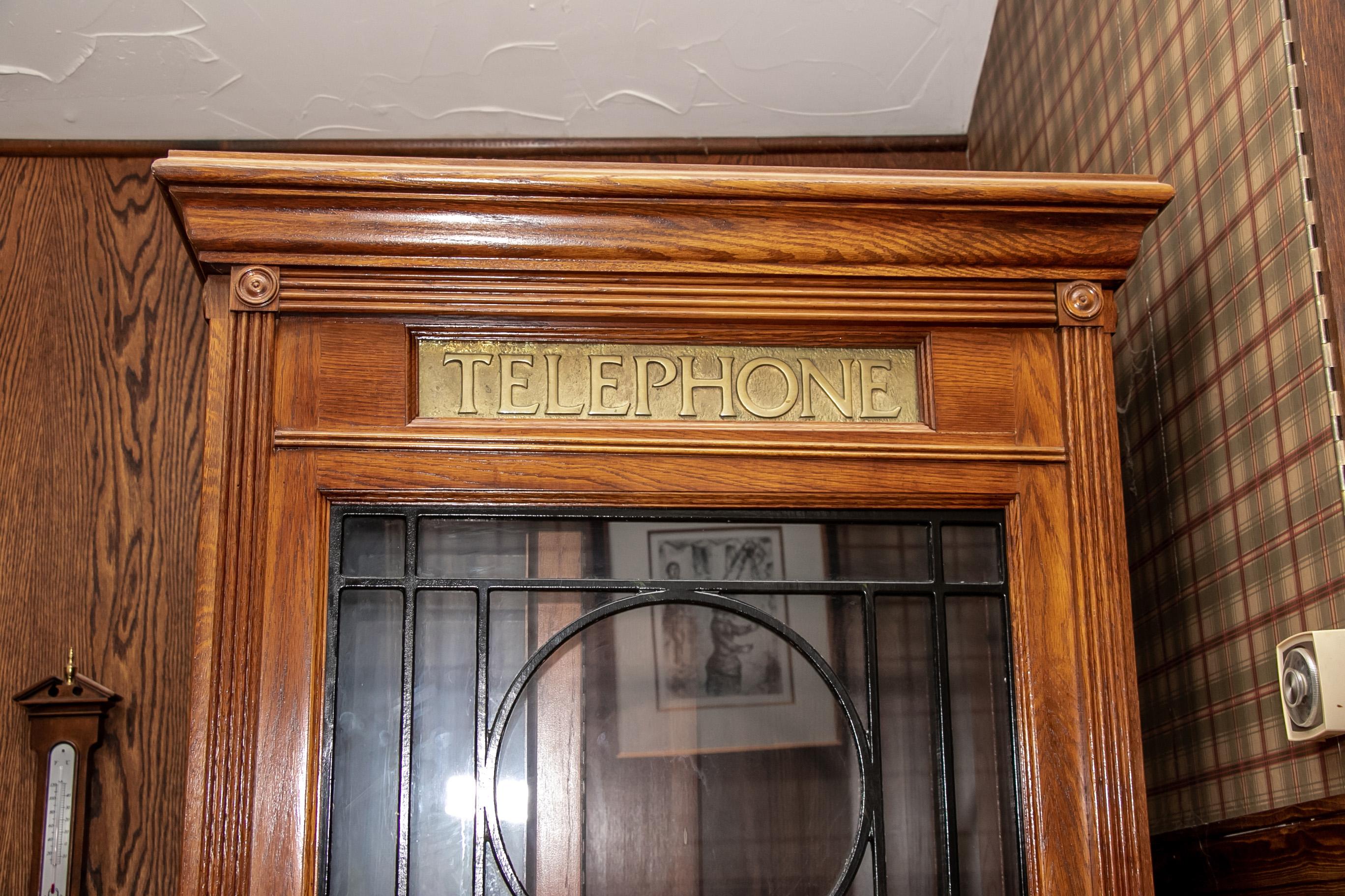 Vintage working replica of an antique wood and glass door phone booth, the original circa 1910. Replica made by the Pulaski Furniture Corp., VA. With an oak case with reeded supports and tops on three sides and a carved cornice. The front folding