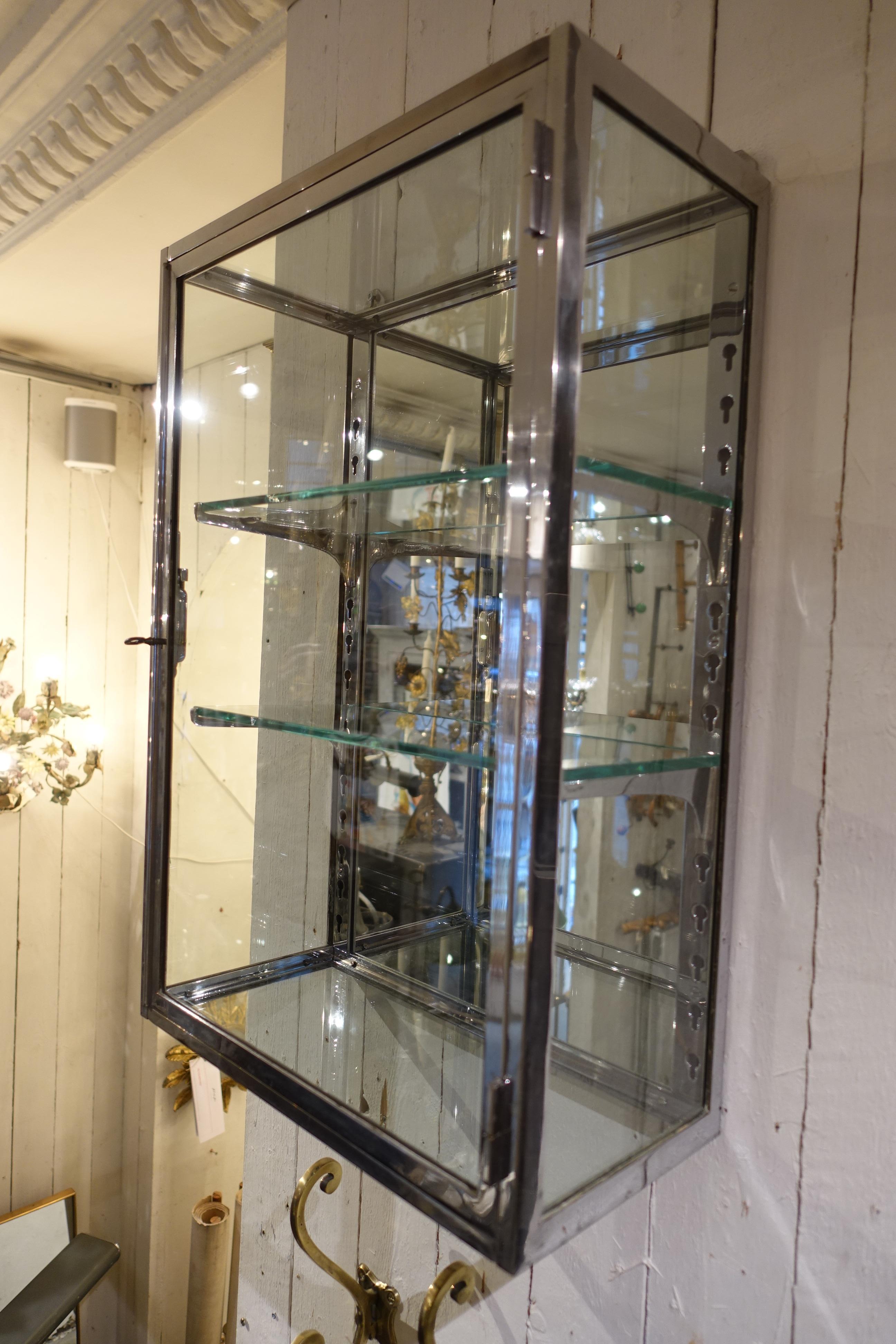 Gorgeous French Art Deco wall vitrine cabinet. Chrome coated brass, with accompanying key and two glass shelves, as well as adjustable shelf brackets and mirrored backing. Provenance – part of a boutique’s inventory, from circa 1930. Great