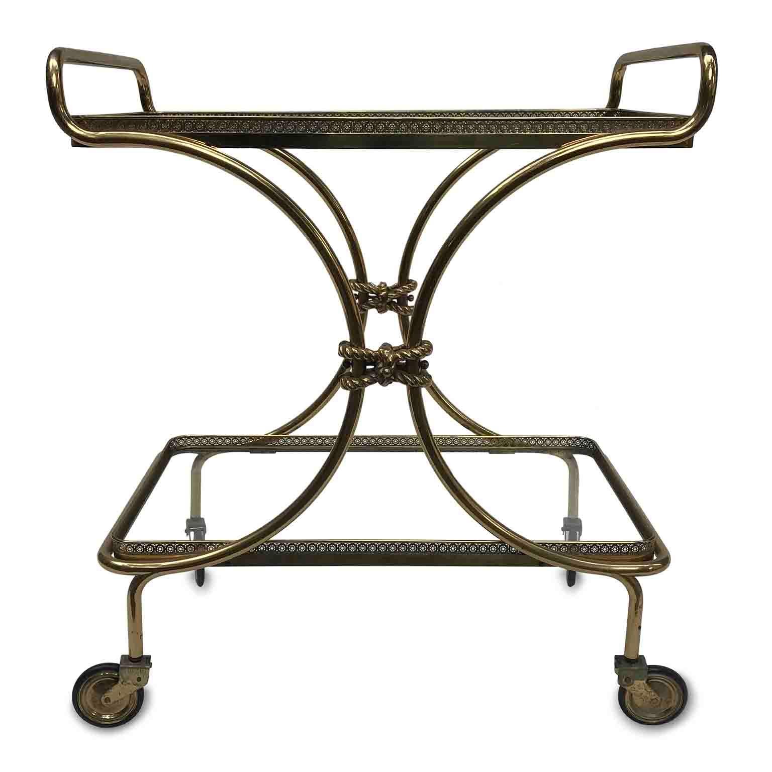 Mid-20th century Italian two-tiered brass bar cart in good condition with two crystal shelves surrounded by lovely pierced brass banisters. 
The side crossed tubes of the rectangular frame structure are joined by two cast brass elements in the shape