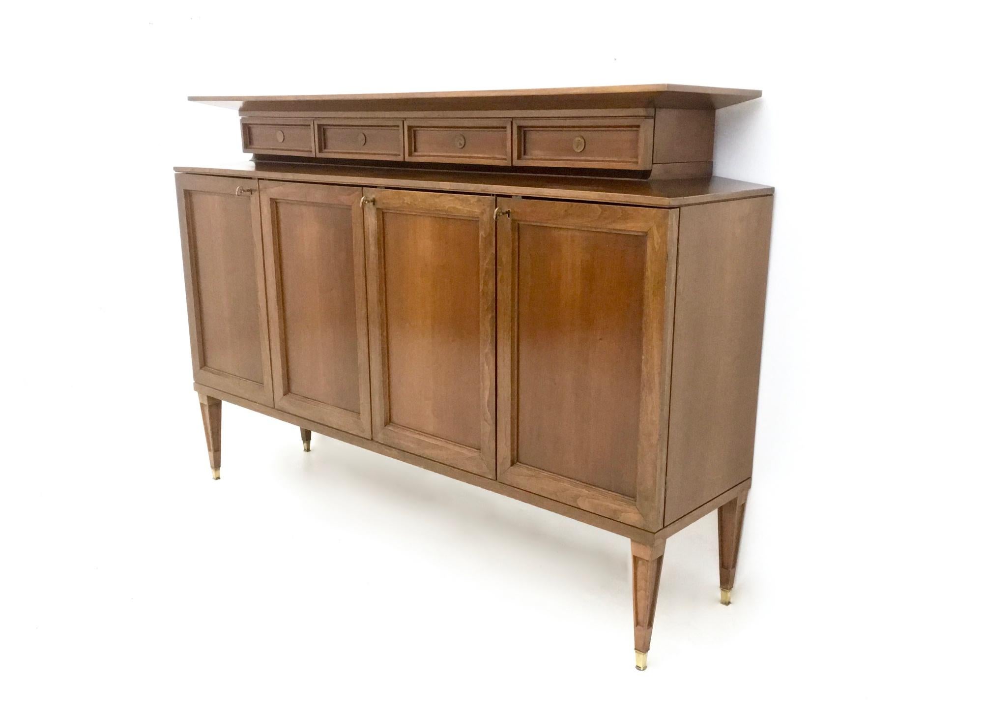 1950s. 
This cabinet is made in walnut and features brass details, walnut interiors and glass shelves. 
It is a vintage piece, therefore it might show slight traces of use, but it can be considered as in excellent original condition and ready to