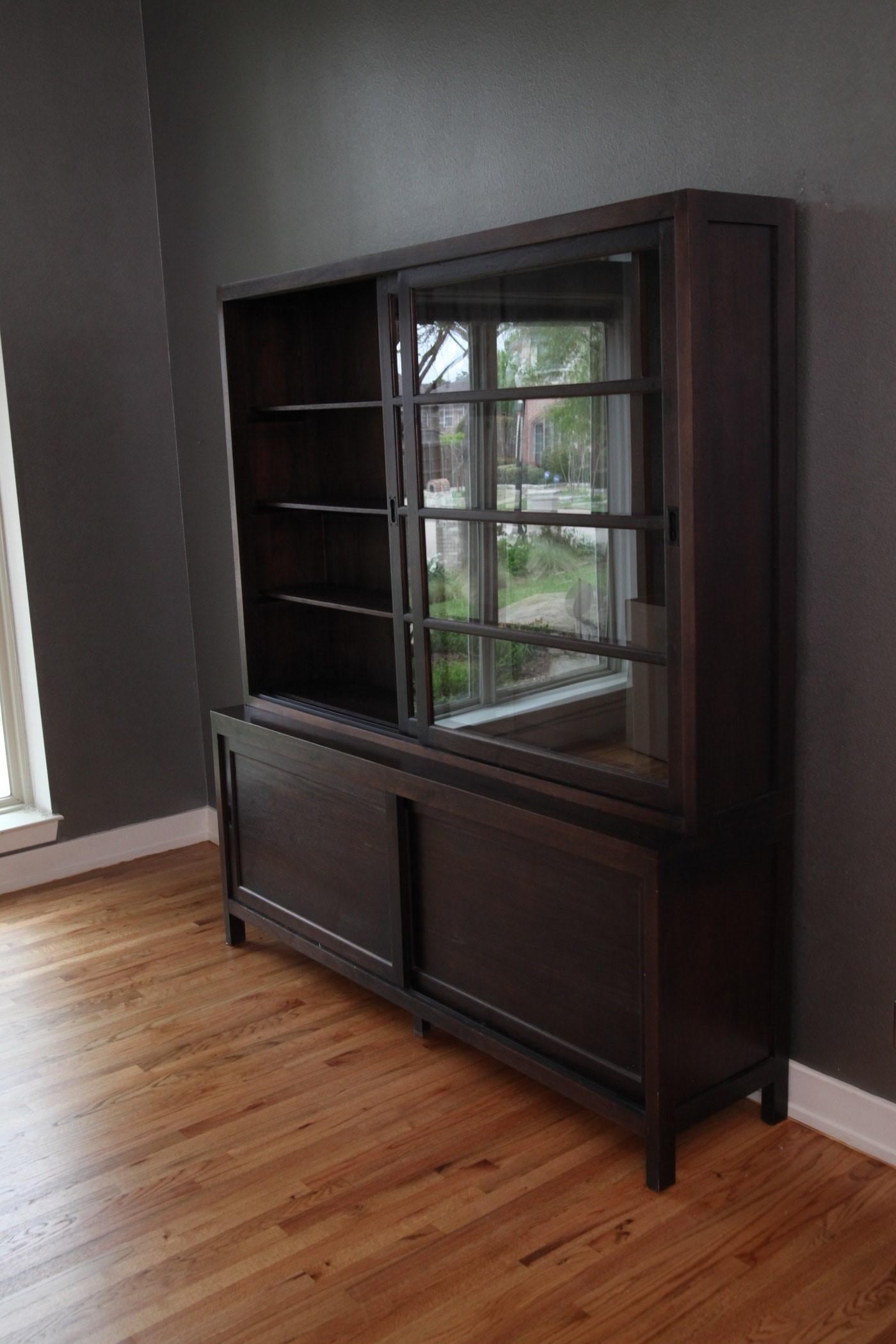 This handsome ebonized Bibliotheque comes in two parts; the upper bookcase boasts two glass front upper sliding doors that close before adjustable shelves. The glass front display and closed storage is both functional and highly decorative. The