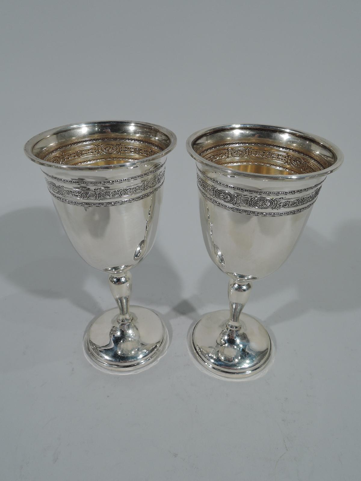 Pair of neoclassical sterling silver goblets. Each: Ovoid bowl, baluster stem, and raised round foot. Chased and repoussé ornamental bands with leaf-and-dart, paterae, and scrollwork. Gilt interior. Hallmarked M. Fred Hirsch, a Jersey City maker