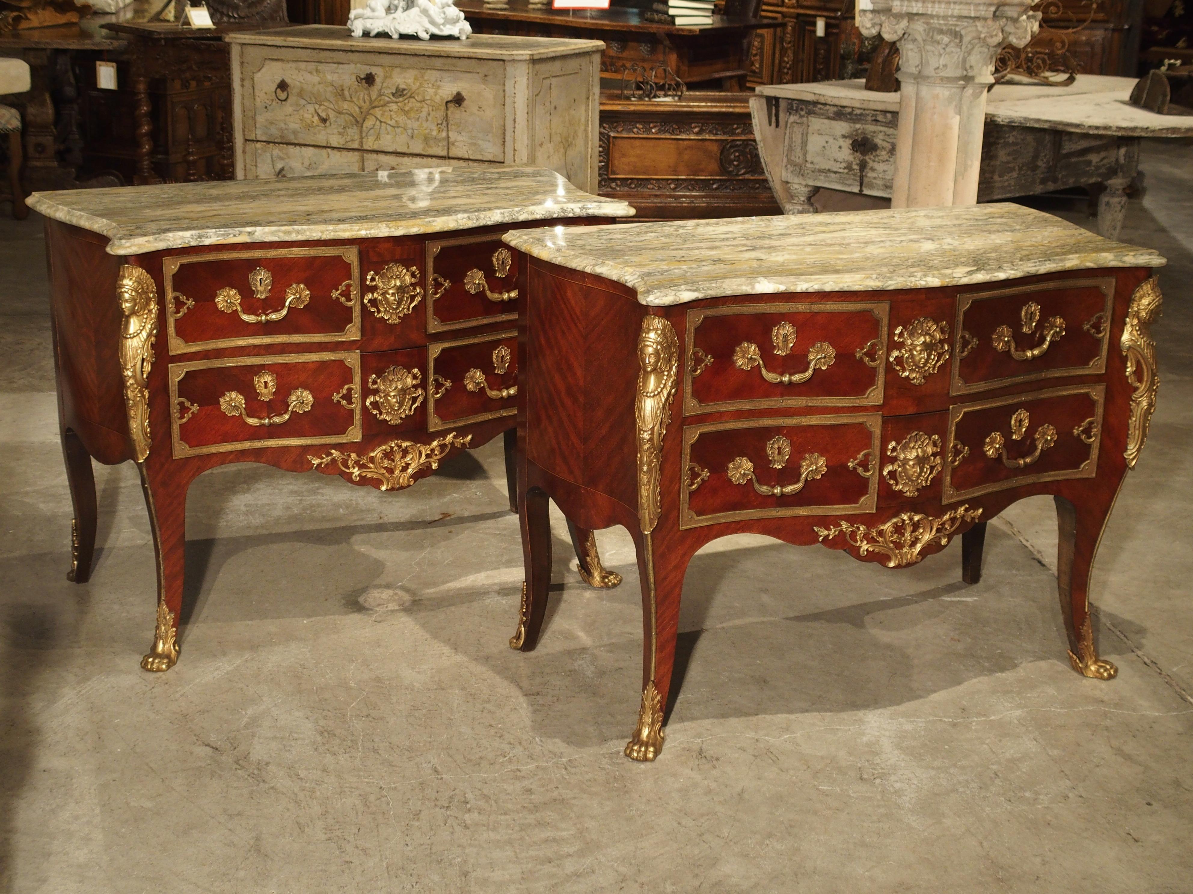 This elegant pair of Louis XV style mahogany commodes are from the workshops of Spain, sometime in the early 20th century. Each commode has variegated, light colored marble tops and beautiful gilt bronze mounts. Pairs of Louis XV style commodes of