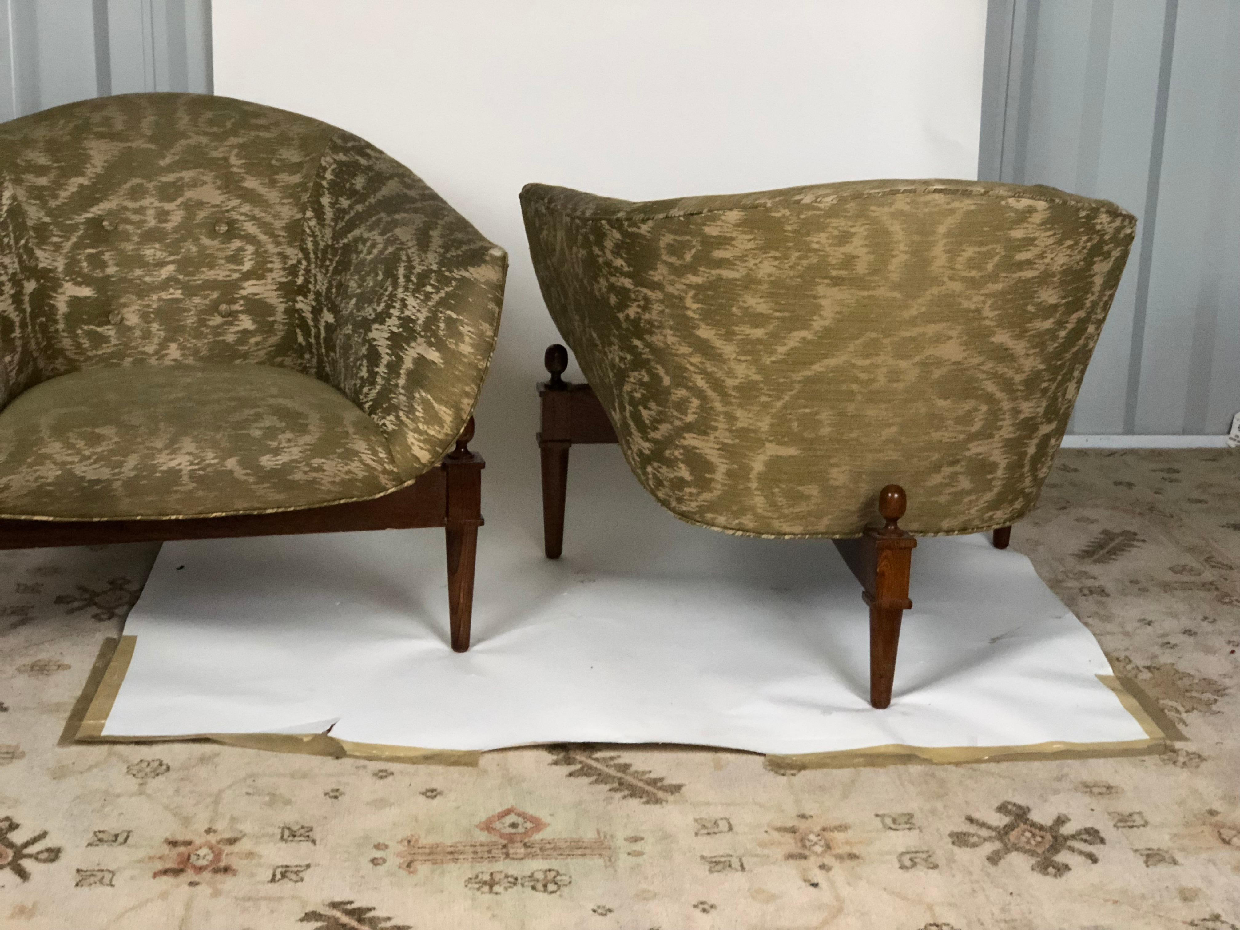 Pair of midcentury style Mimi club chairs on wooden tripod platforms with upholstered tufted seats. Made by Global Views. Measures: Seat height is 16 inches and the arm height is 23 inches.
