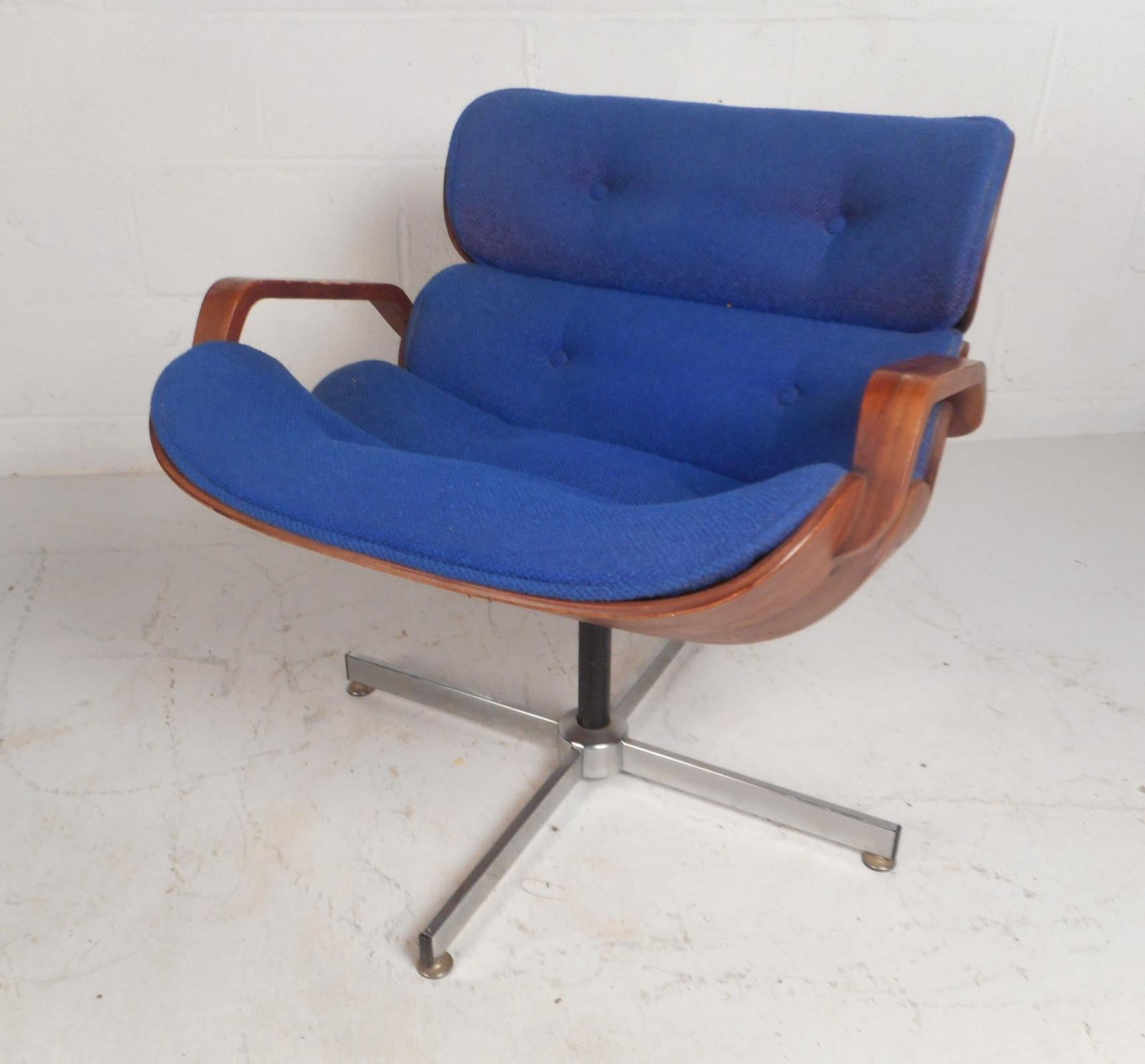 A beautiful vintage modern lounge chair that swivels and tilts ensuring maximum comfort. This unique chair features thick padded seating covered in plush blue tufted fabric. Sleek design with a hardshell walnut frame, sculpted wood arm rests, and