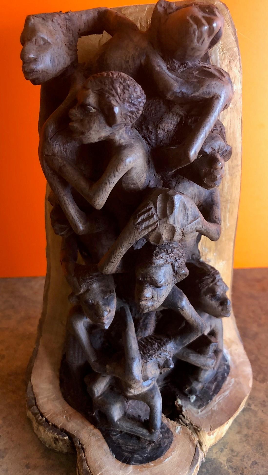 Une sculpture africaine unique représentant huit villageois au travail et au jeu. La pièce est sculptée à la main dans une branche d'arbre dont les couches internes sont en bois foncé et les couches externes en bois clair. C'est vraiment une pièce