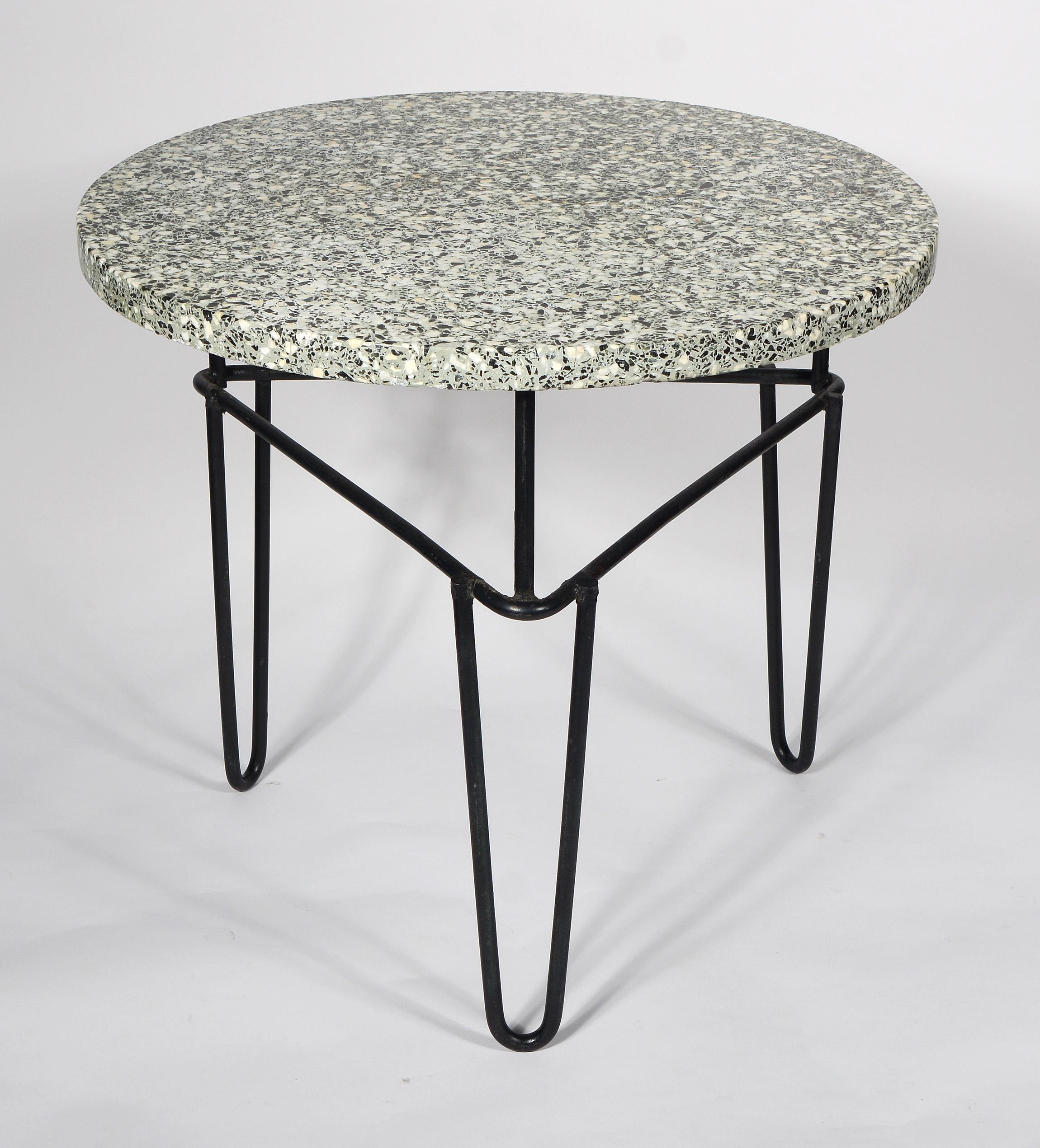 Wrought iron side table with a green terrazzo top. This has a triangular base with hairpin legs and three vertical supports for the top. The top is not attached and just rests on the base. There are some losses on the edge of the top. The majority