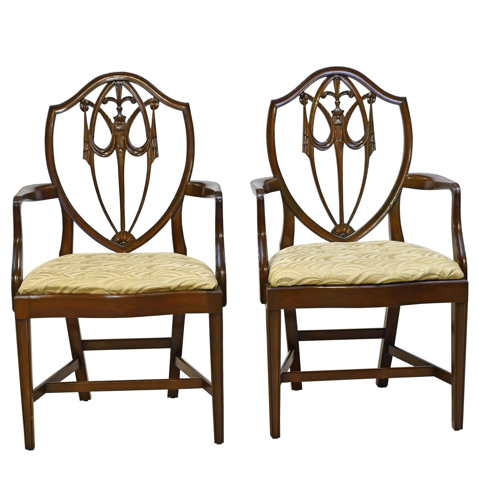 A beautiful set of twelve (12) American dining chairs in solid mahogany comprising of two armchairs and ten side chairs in the Hepplewhite-style with a shield-back with carved fleur-de-lis and swags on the pierced back, and a serpentine front with