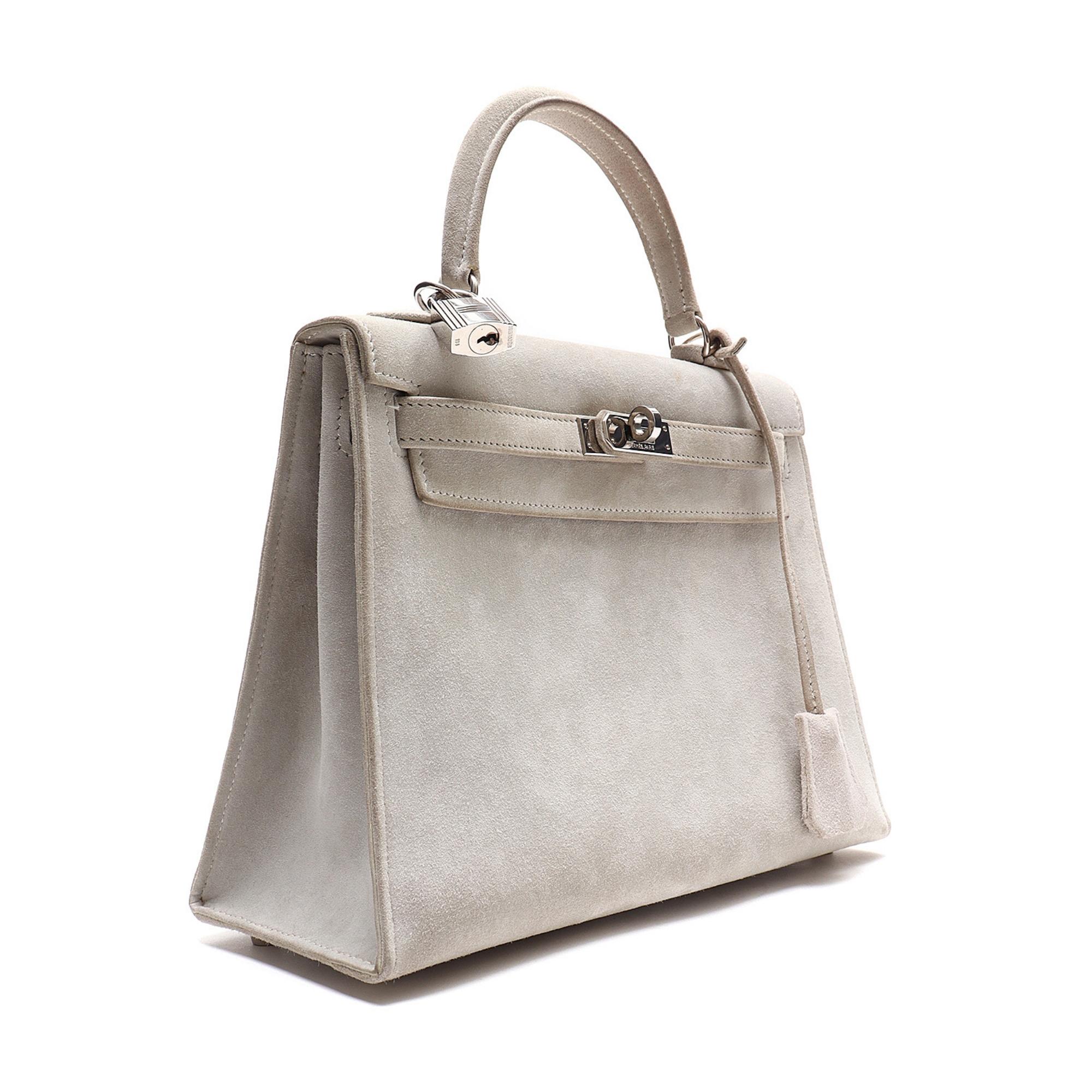 This iconic and classic handbag is constructed of suede in high grey Doblis. The bag features a sturdy suede top handle, an optional shoulder strap, and a crossover flap and strap closure with a silver plated signature Kelly turn lock and padlock