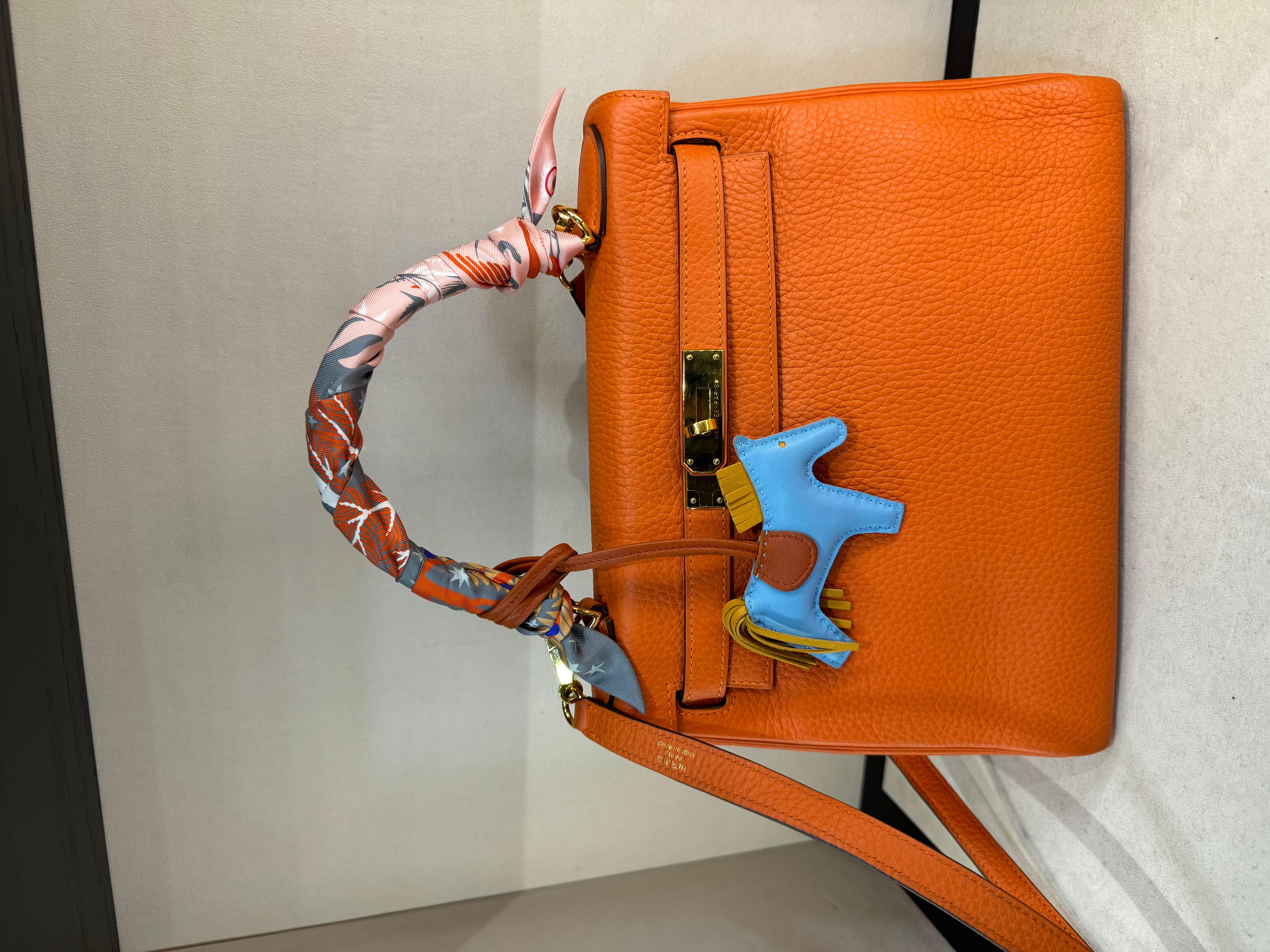 Hermes Kelly 28 Orange Taurillion Clemence Leather Gold Hardware Retourne Bag.
Such a desirable bag for a classic Hermes look, with the gold hardware even more rare. 

The Kelly is known for its simple design and unmatched elegance. The top handle